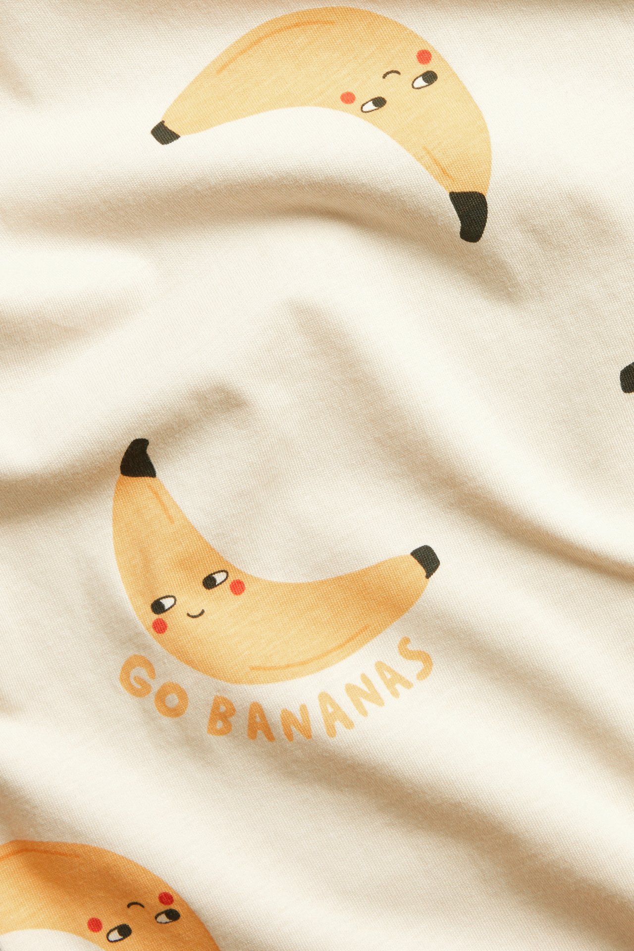 Zbliżenie beżowego bawełnianego t-shirtu z powtarzającym się wzorem bananów i napisem 'GO BANANAS'.