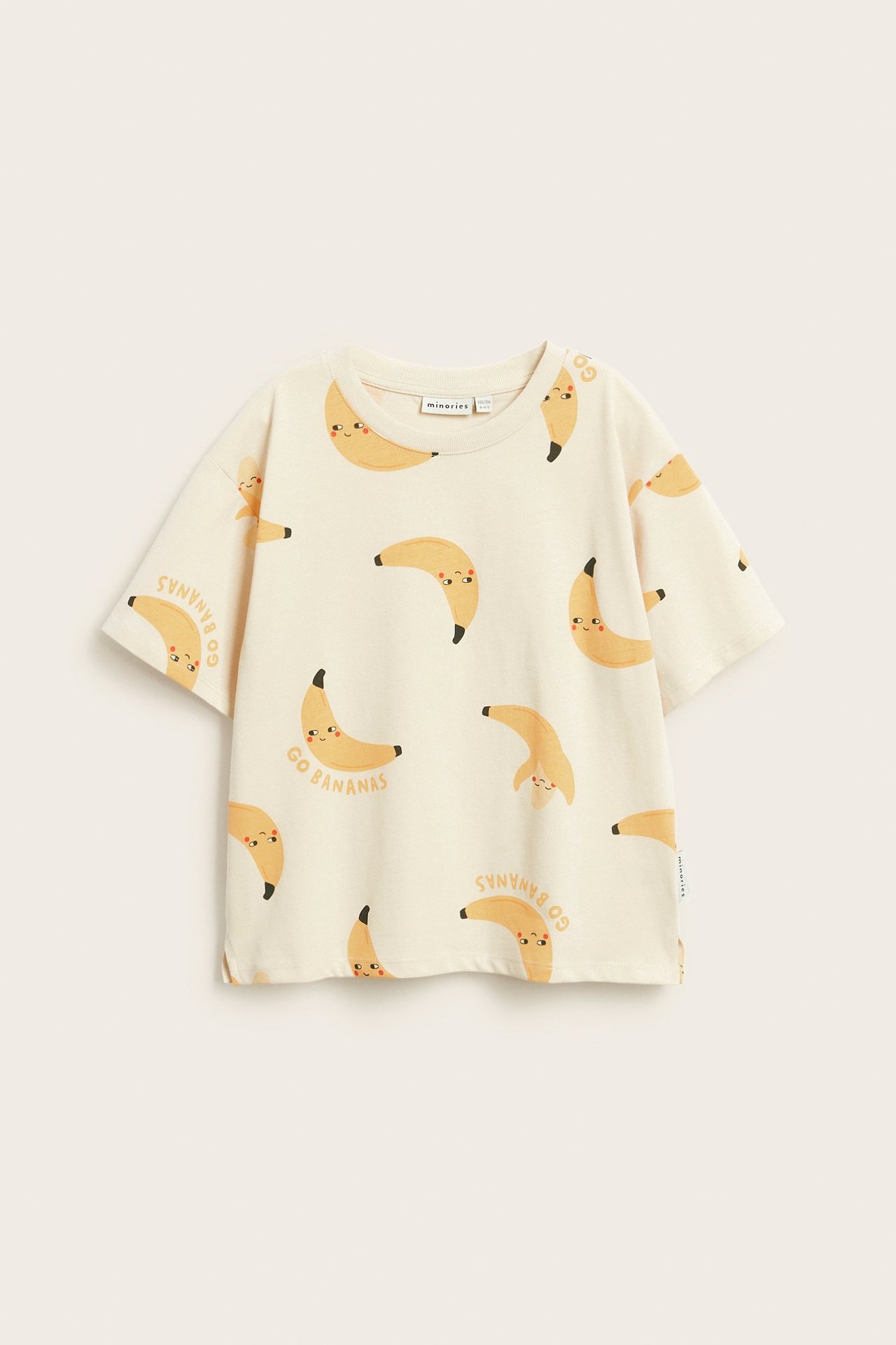 Framsida av en beige bomulls t-shirt med tryck av leende bananer och texten 'GO BANANAS'.