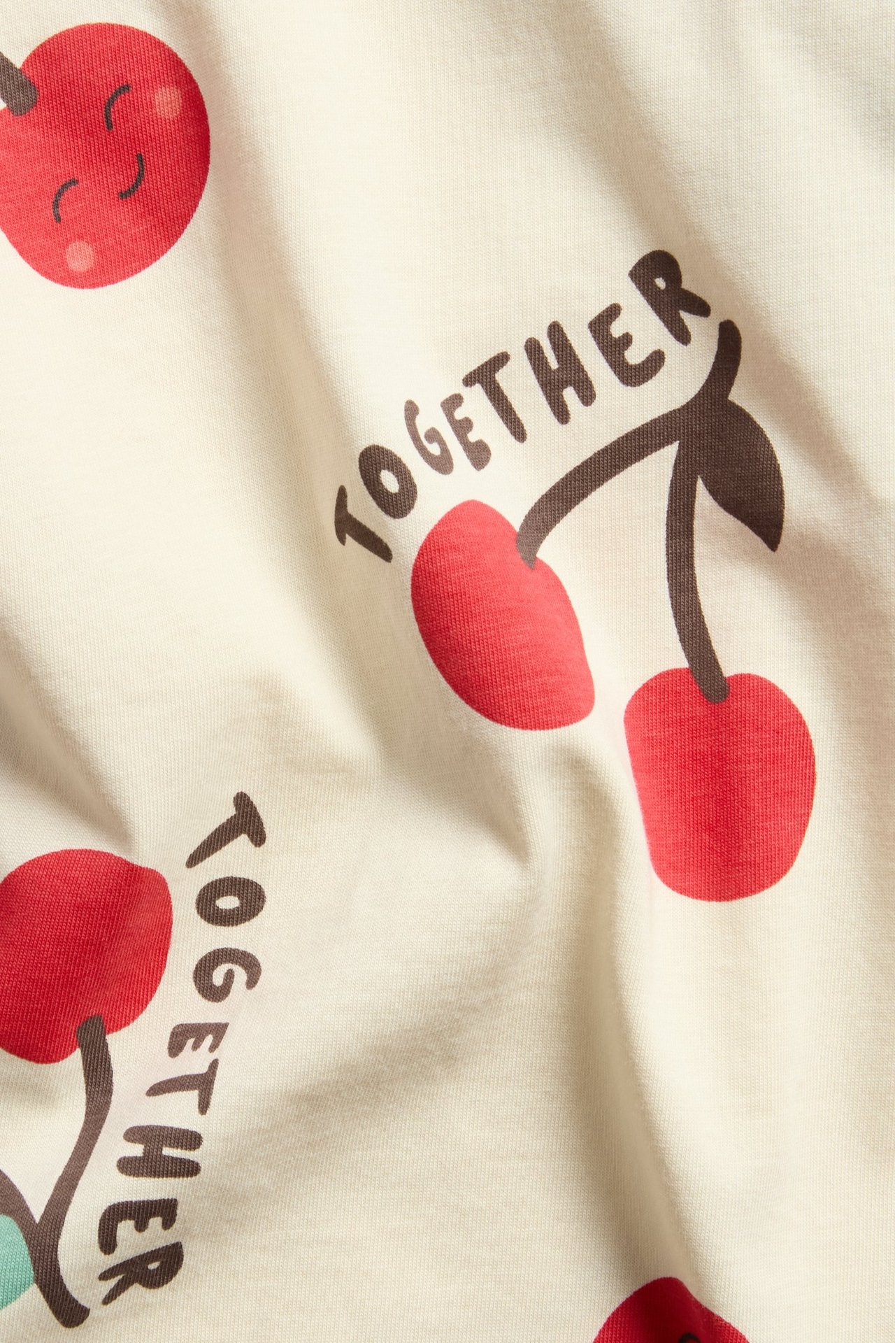 Närbild på en gräddvit t-shirt i bomull för barn med rött körsbärs- och 'TOGETHER'-tryck.