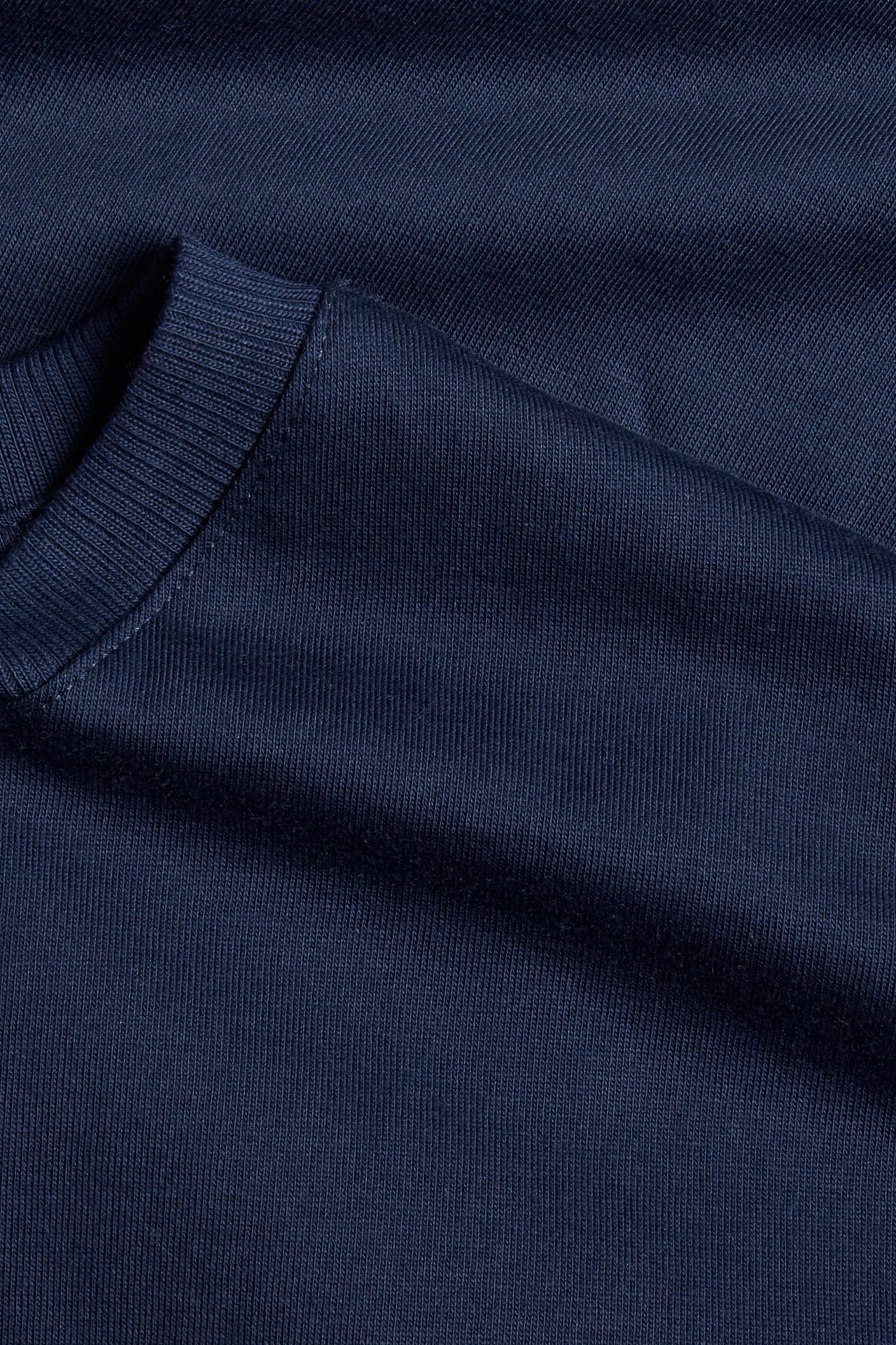 Nærbilde av en ensfarget marineblå t-skjorte i bomull med ribbet rund hals.