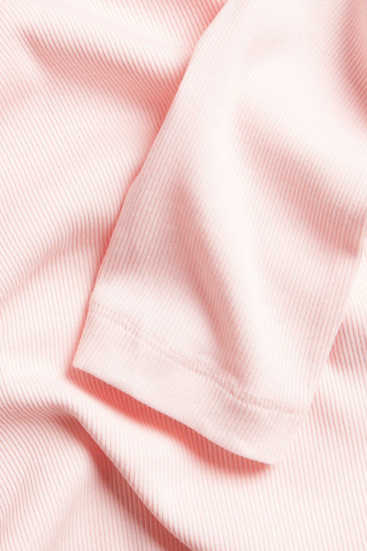 Zbliżenie jasnoróżowego prążkowanego topu z długim rękawem.