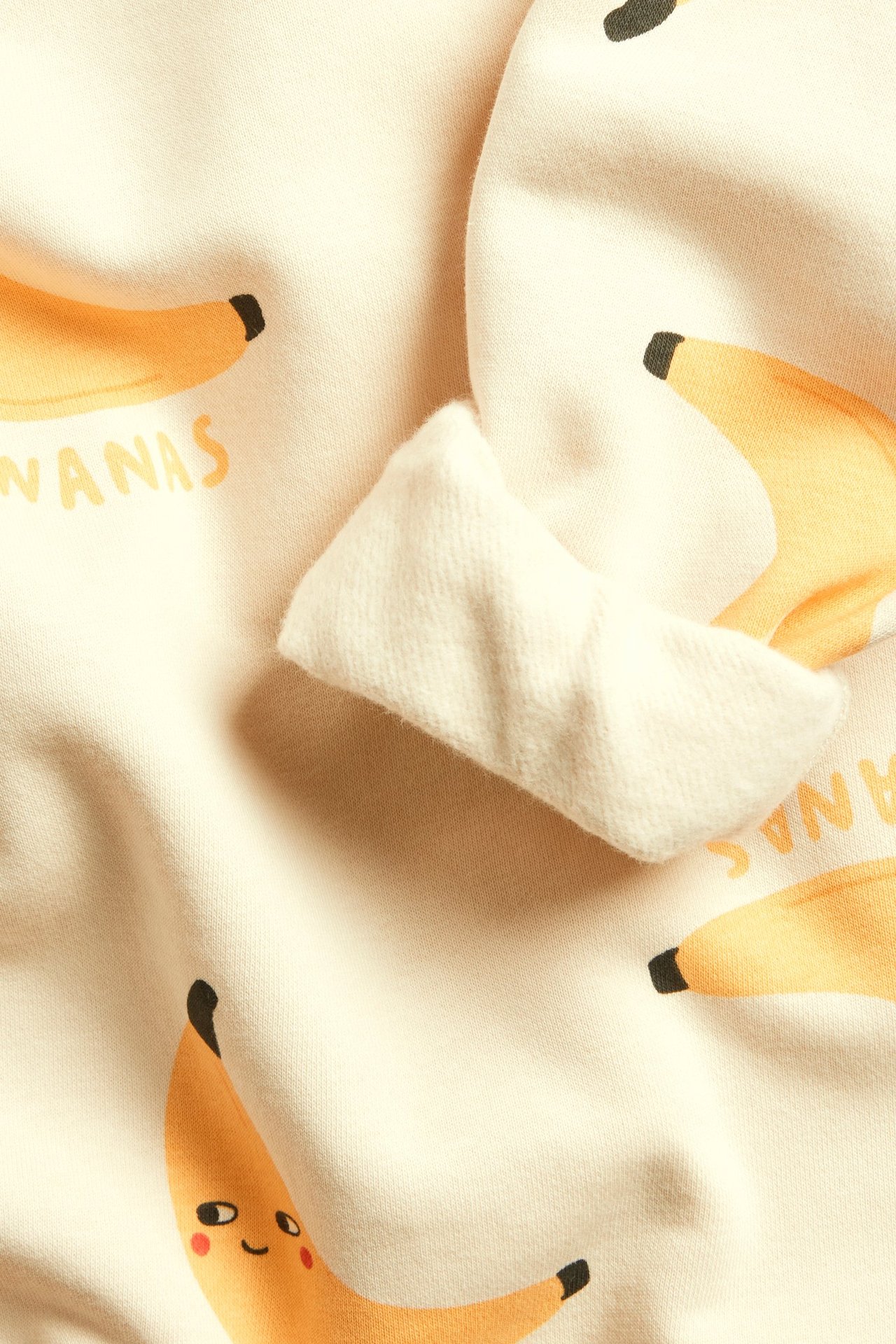 Zbliżenie na beżową bluzę z nadrukiem bananów i tekstem 'BANANAS', z widocznymi ściągaczami.