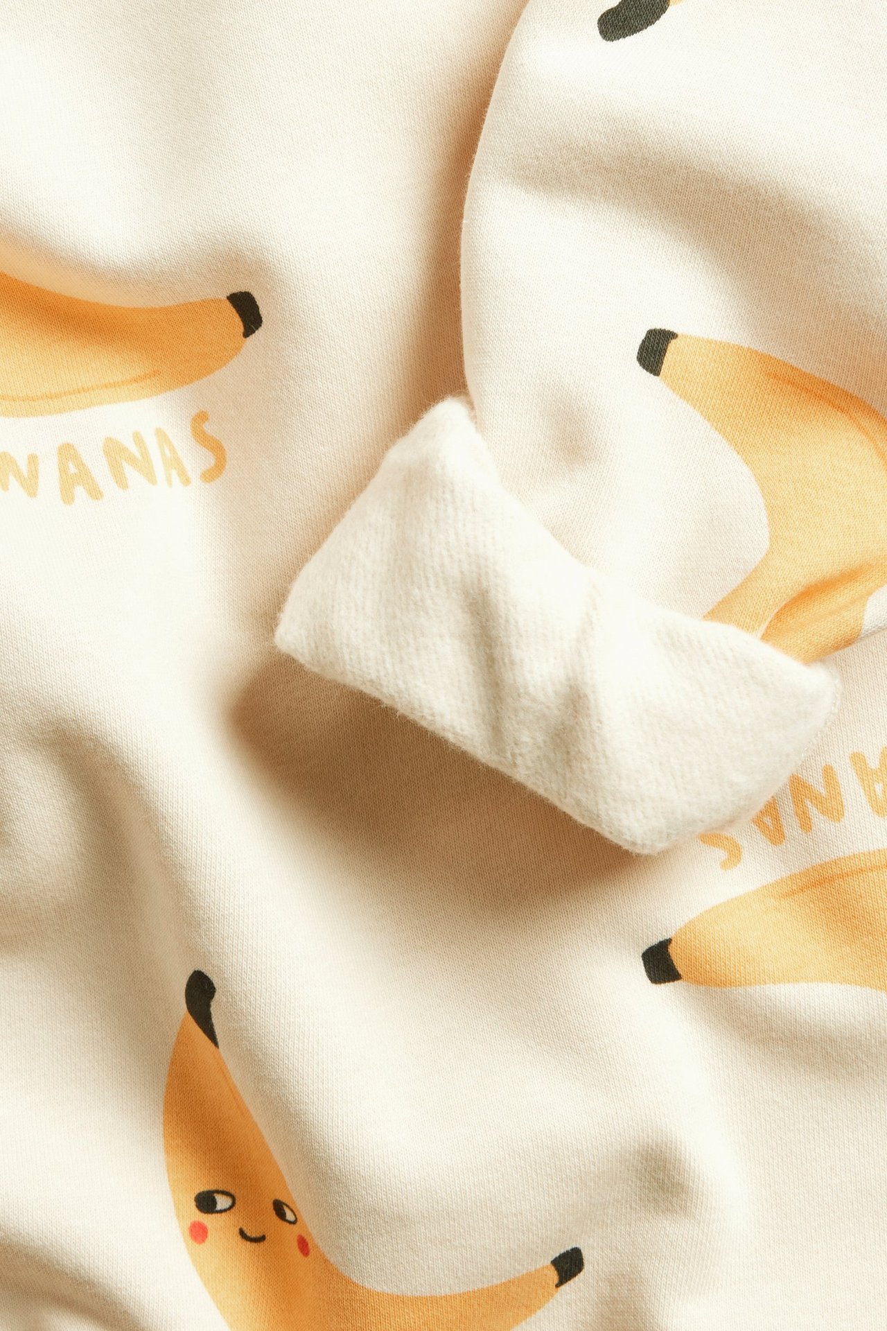 Zbliżenie beżowej dziecięcej bluzy z nadrukiem bananów i widocznymi ściągaczami.