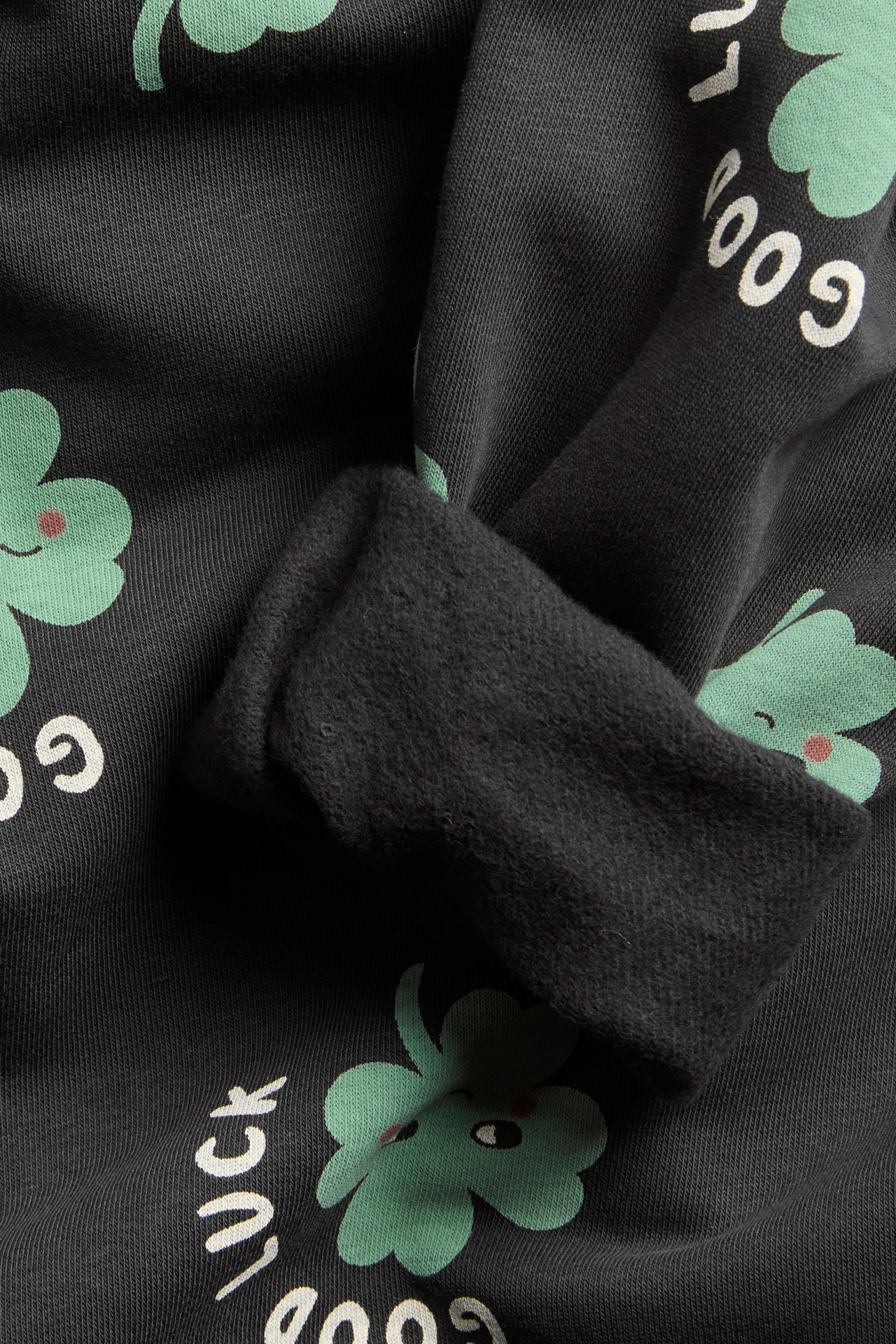 Lähikuva mustasta collegepaidasta, jossa vihreitä apiloita ja valkoinen 'GOOD LUCK' -teksti, näyttäen resorin.