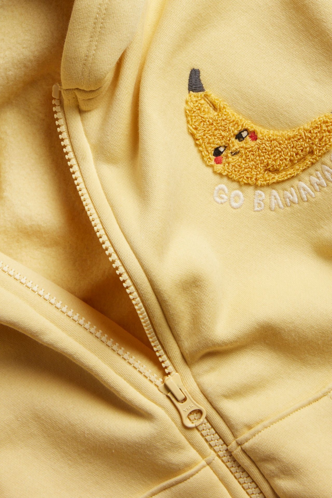 Zbliżenie żółtej dziecięcej bluzy z kapturem, z zamkiem i haftem frotte z bananem na piersi.
