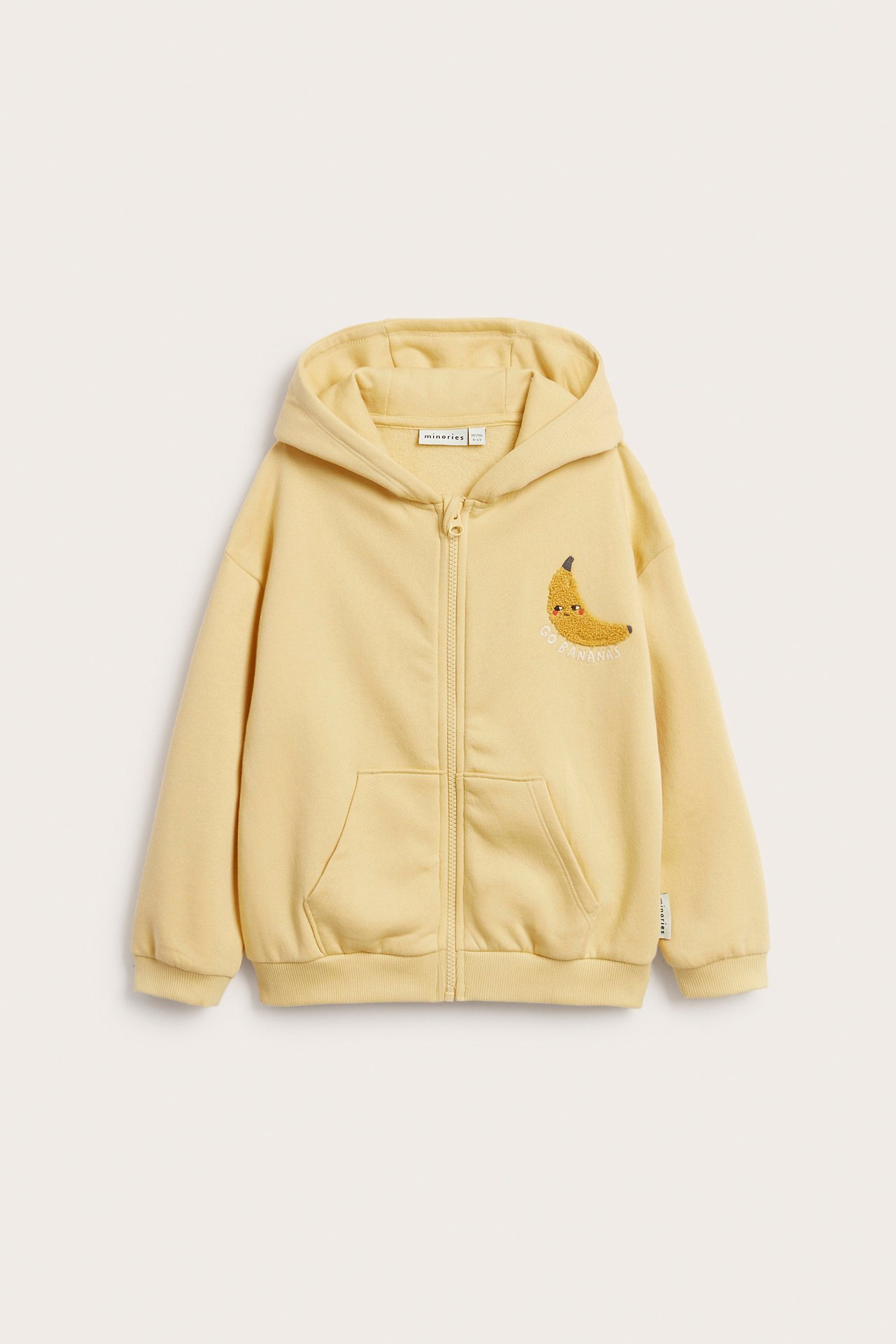 Edestäpäin, lasten keltainen huppari vetoketjulla, etutaskuilla ja frotee-banaanikirjonnalla.