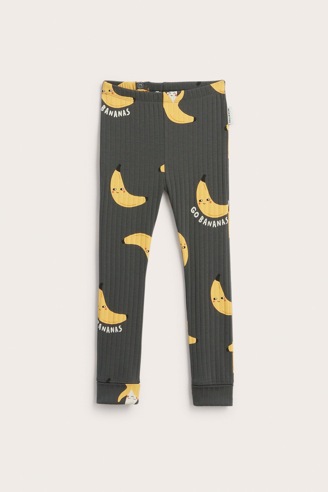 Edestä tummanharmaat ribatut lasten leggingsit keltaisella banaanikuviolla ja käännettävillä lahkeensuilla.
