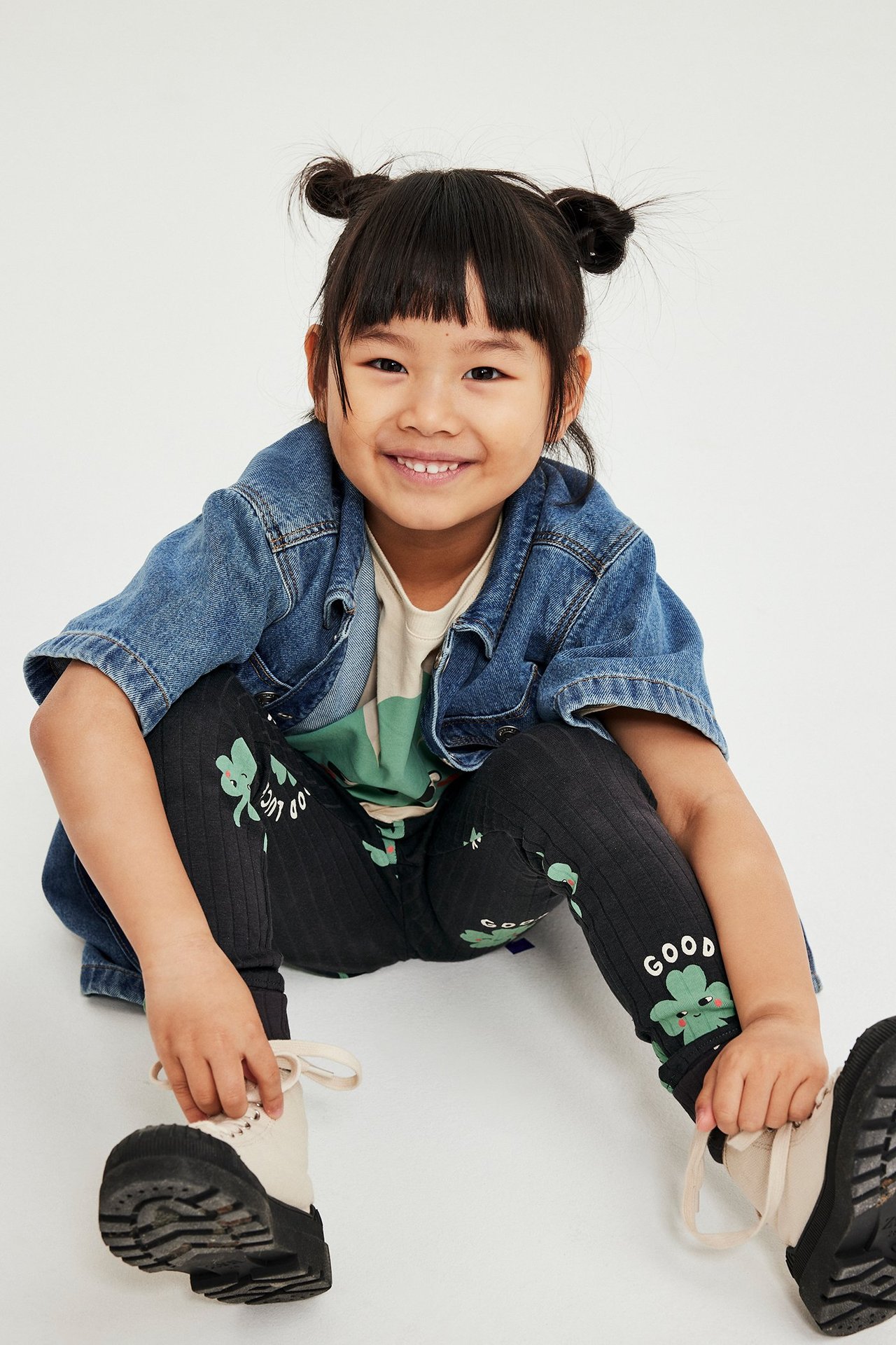 Edestä: Lapsi mustissa ribatuissa apila-kuvioisissa leggingseissä, beigessä t-paidassa ja farkkutakissa.