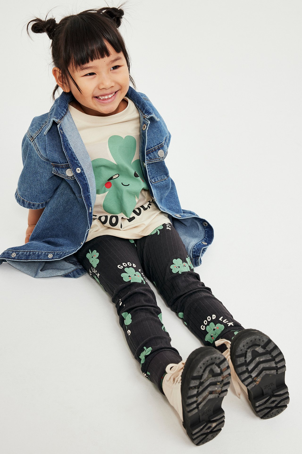 Edestä: Lapsi yllään mustat ribbileggings apilaprintillä, beige t-paita ja sininen farkkutakki.