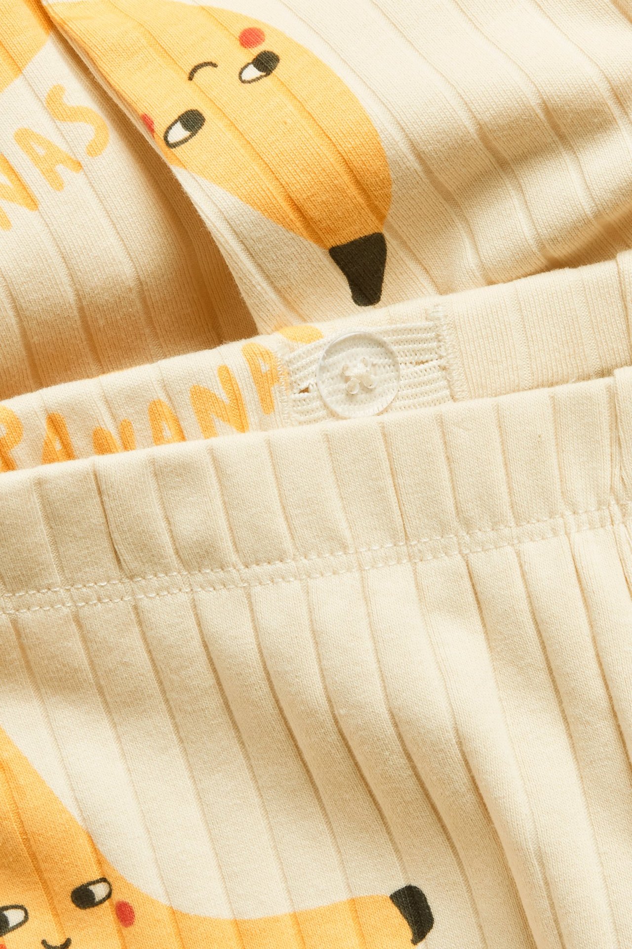 Lähikuva beigenvärisistä ribatuista lasten leggingseistä, joissa on banaanikuvio ja säädettävä vyötärönappi.