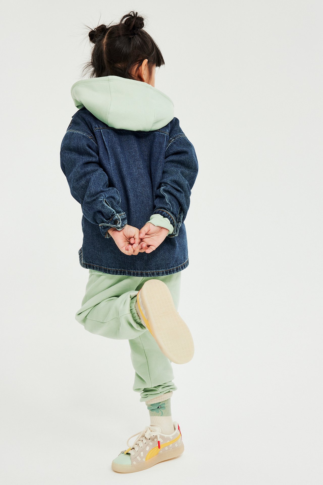 Tylny widok: Dziecko w jasnych zielonych dresach, bluzie, dżinsowej kurtce i tenisówkach.