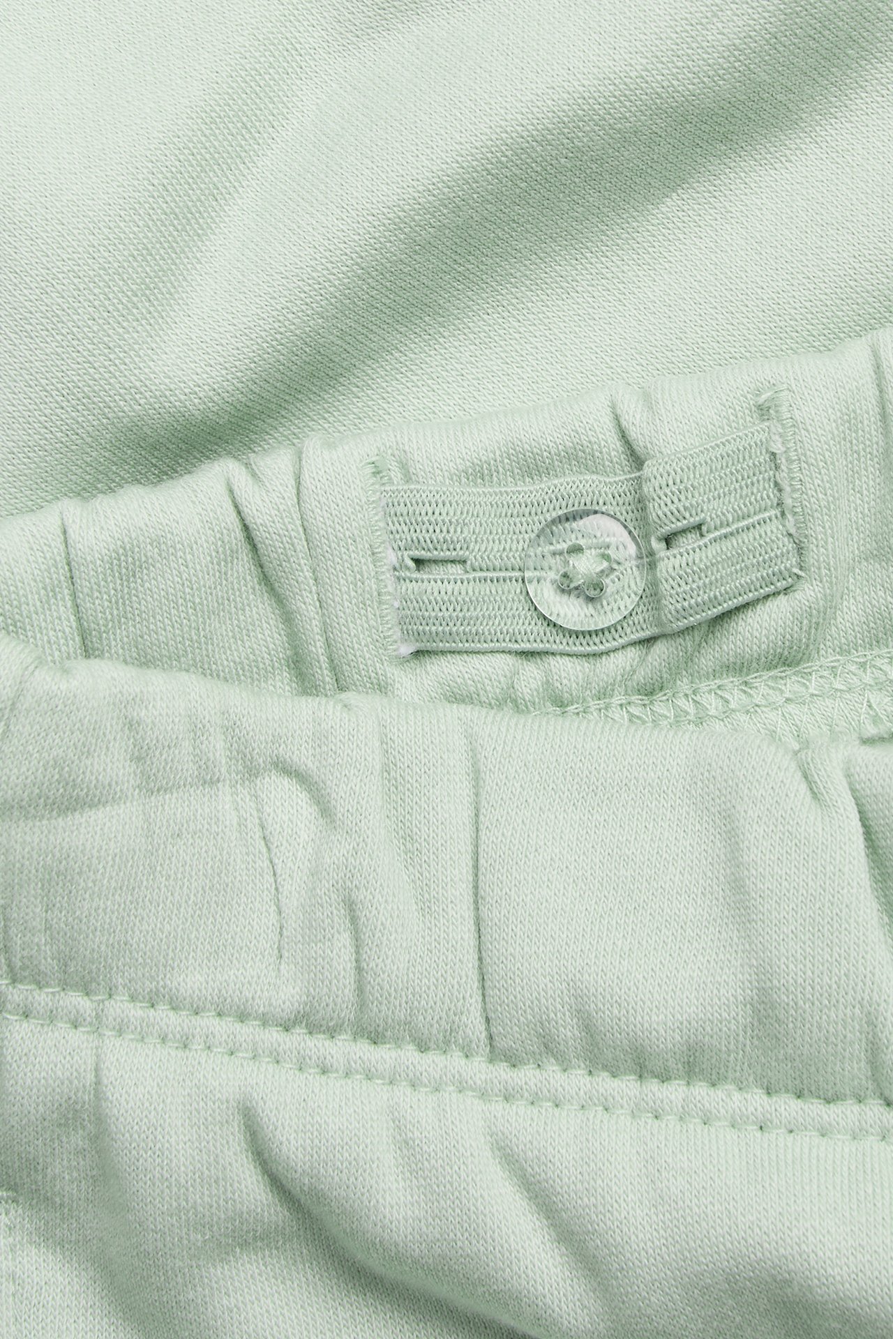 Zbliżenie jasnych zielonych dresów dziecięcych, z regulowanym pasem i przezroczystym guzikiem.