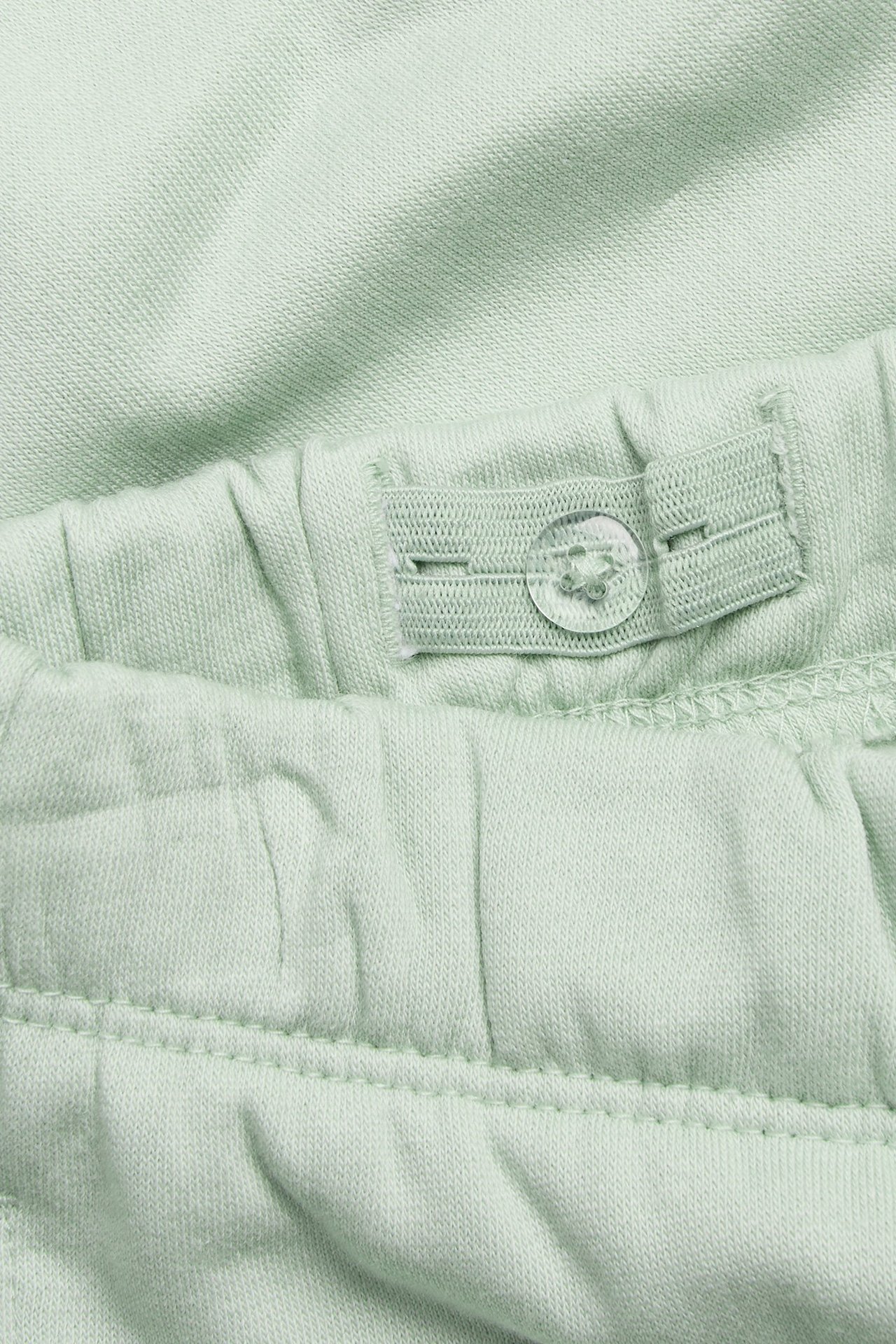 Zbliżenie jasnych zielonych dresów dziecięcych, z regulowanym pasem i przezroczystym guzikiem.