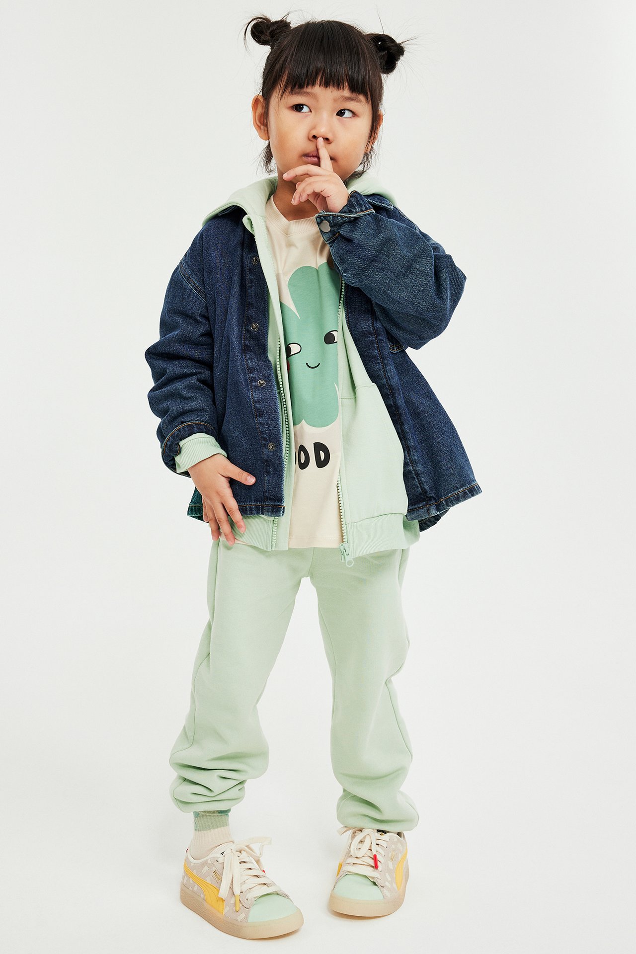 Widok z przodu dziecka w jasnozielonych dresach, jasnozielonej bluzie z kapturem, beżowej koszulce i niebieskiej kurtce.