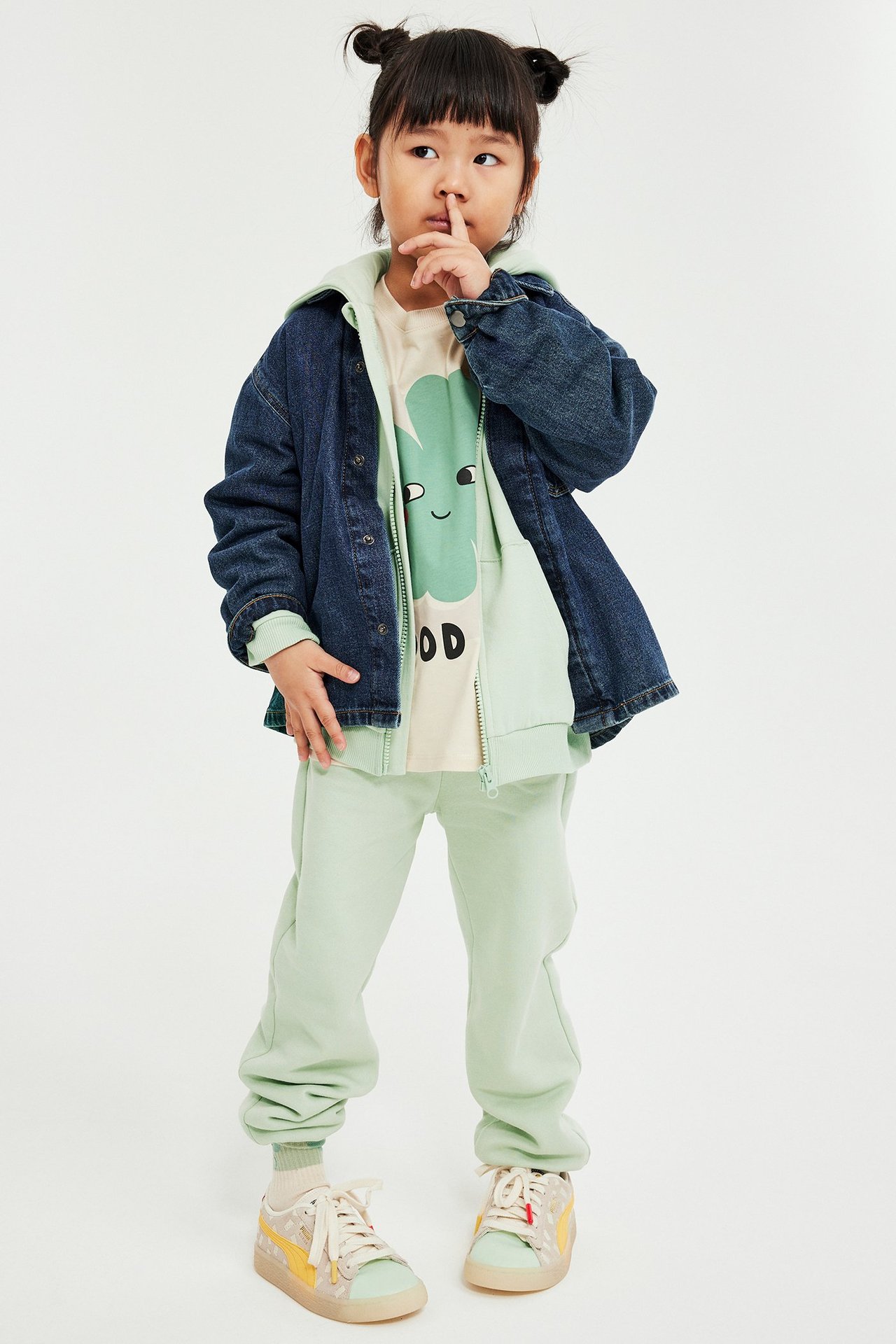 Widok z przodu dziecka w jasnozielonych dresach, jasnozielonej bluzie z kapturem, beżowej koszulce i niebieskiej kurtce.