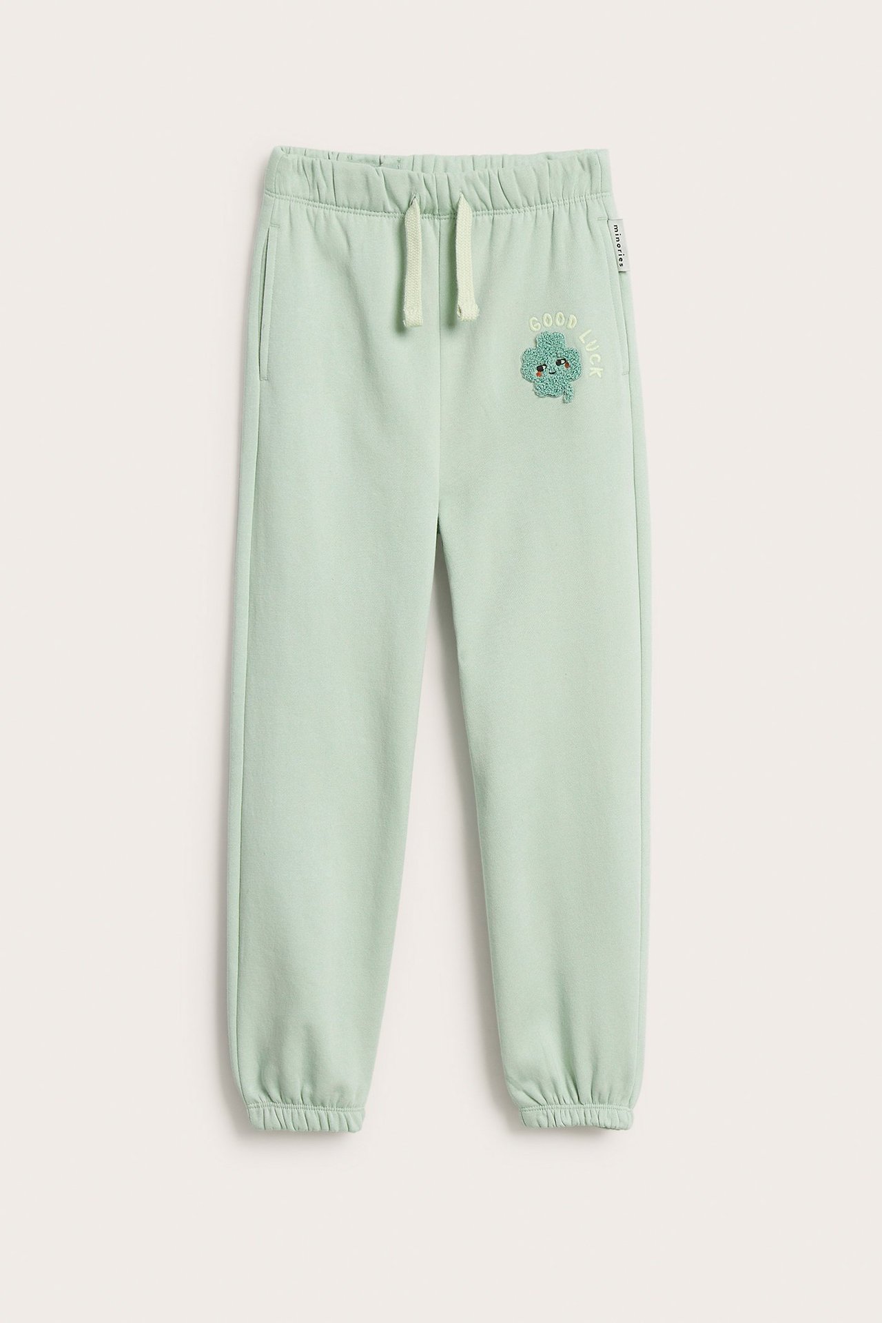 Zielone dziecięce dresy z aplikacją koniczyny, elastyczną talią, sznurkiem i ściągaczami, widok z przodu.