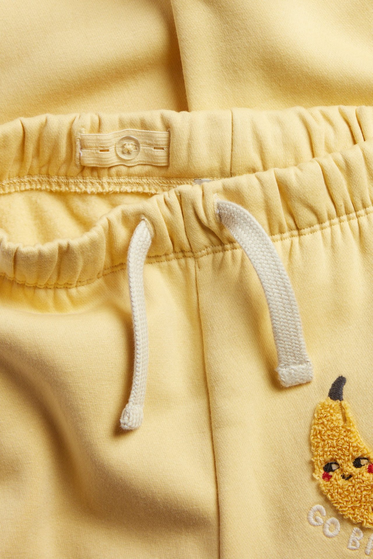 Zbliżenie na żółte dresowe spodnie z mieszanki bawełny ze ściągaczem i teksturowaną aplikacją banana.