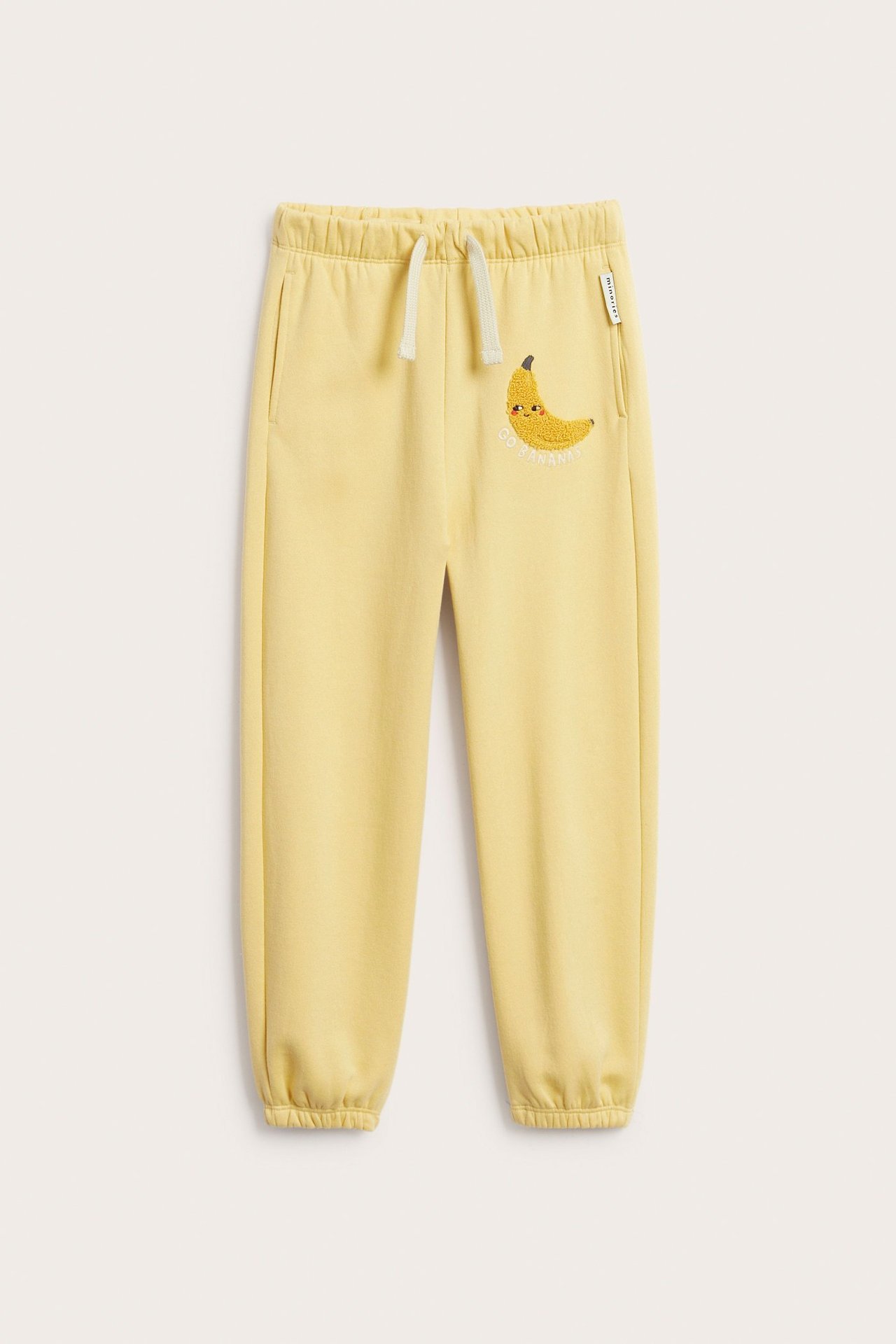 Widok z przodu żółtych dresów dziecięcych z mieszanki bawełny, z elastyczną talią, kieszeniami i aplikacją banana.