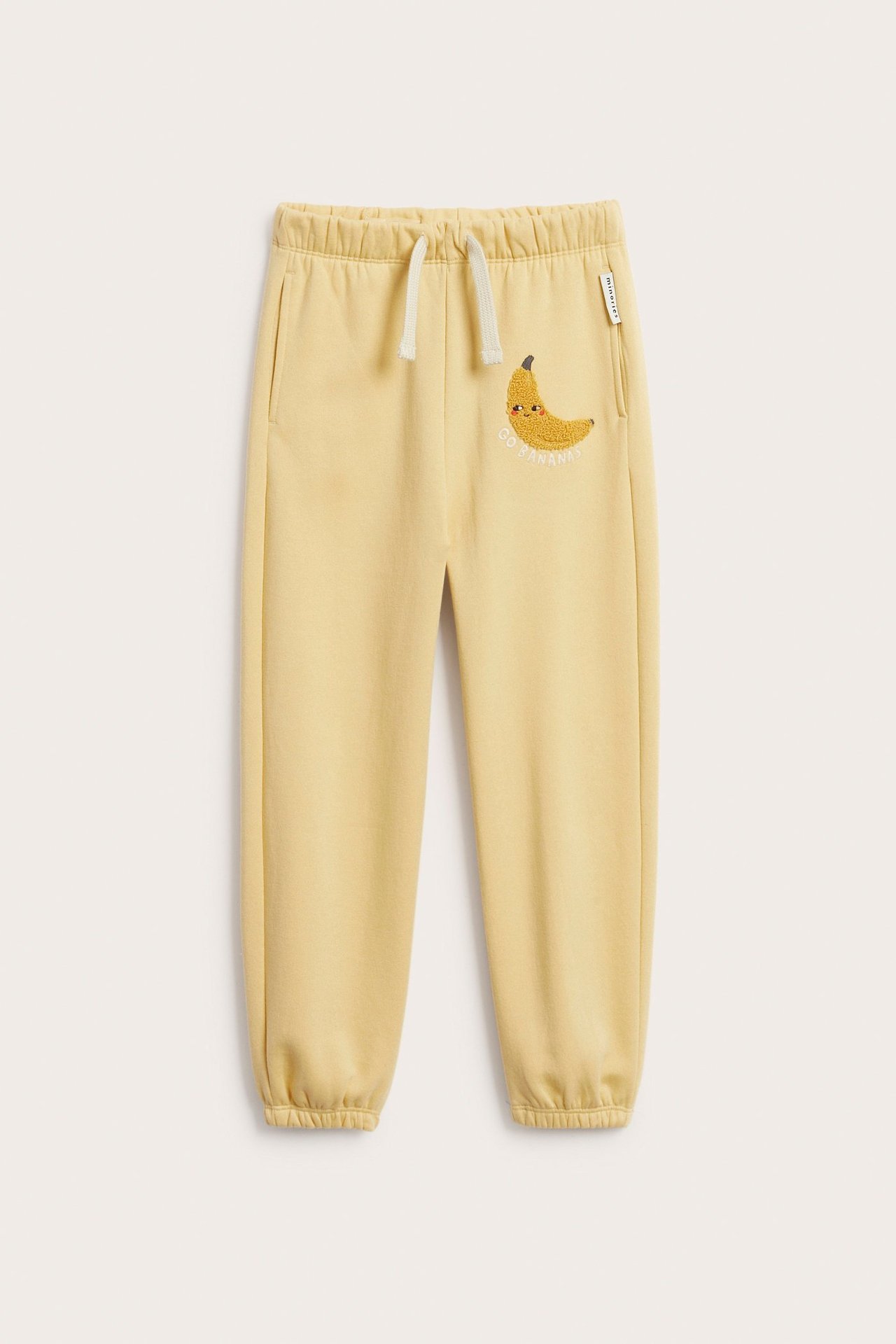 Keltaiset lasten collegehousut, joissa banaaniapplikaatio ja valkoinen kiristysnyöri edestä.