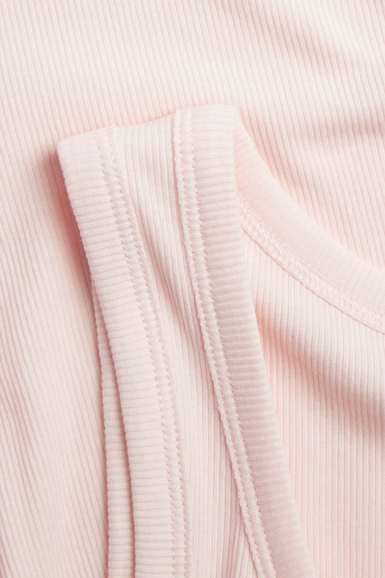 Zbliżenie na jasnoróżowy, prążkowany top, ukazujące strukturalny materiał, ramiączko i dekolt.
