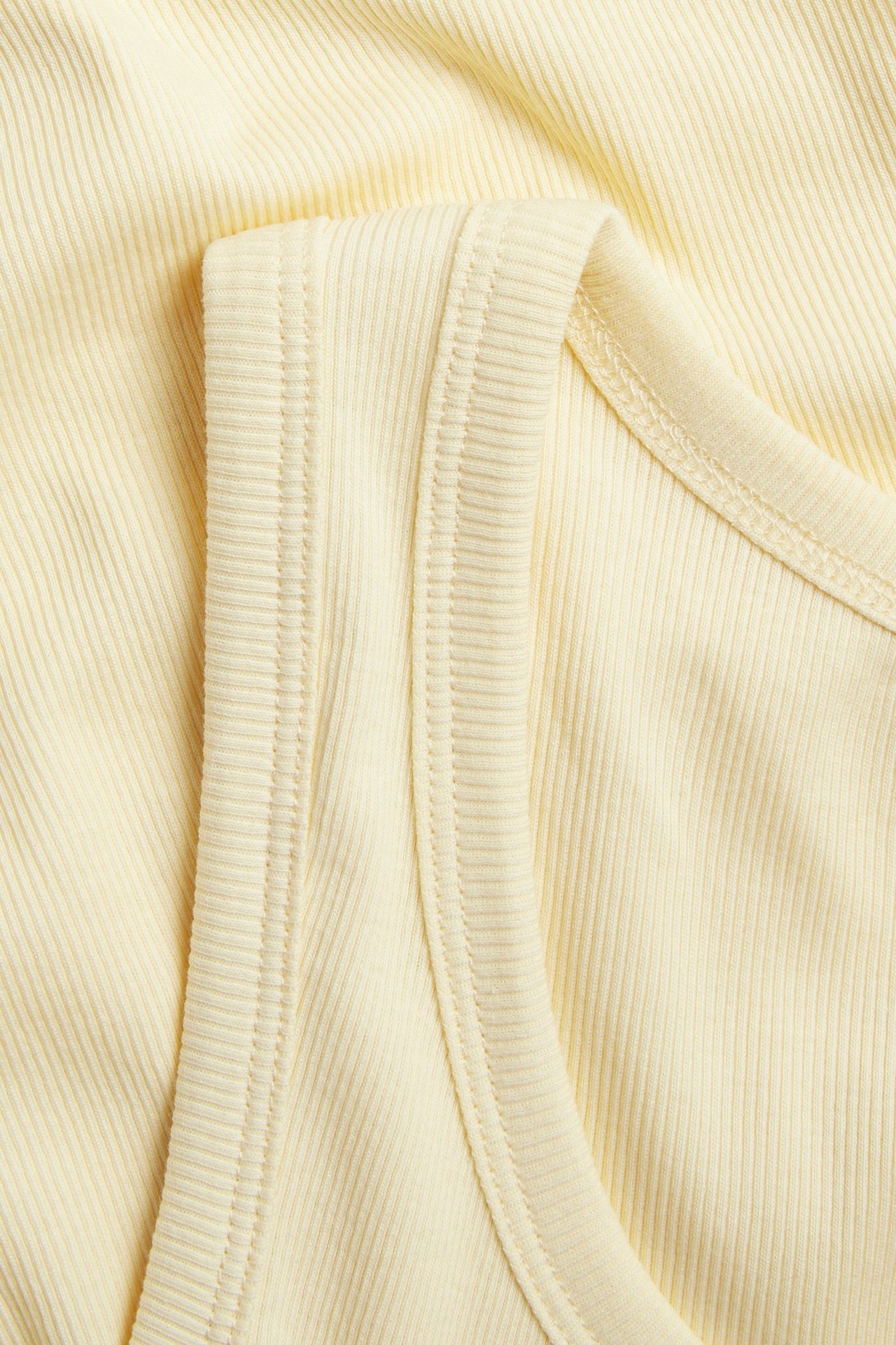 Nærbilde av en lys gul ribbet topp, som viser det smale ribbemønsteret og synlige sømmer.