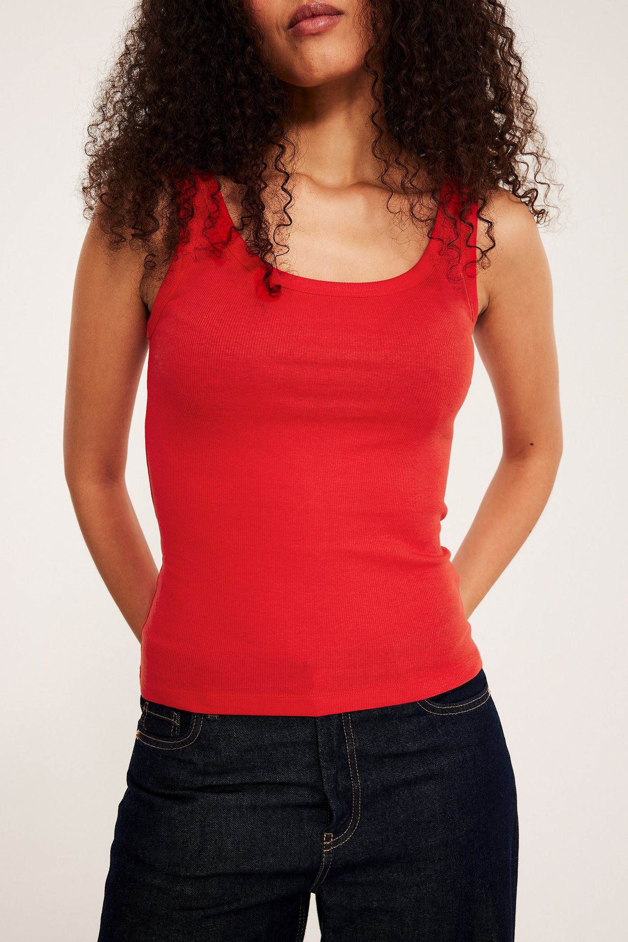 Naisen etunäkymä, yllään punainen istuva ribbitoppi ja tummansiniset farkut.