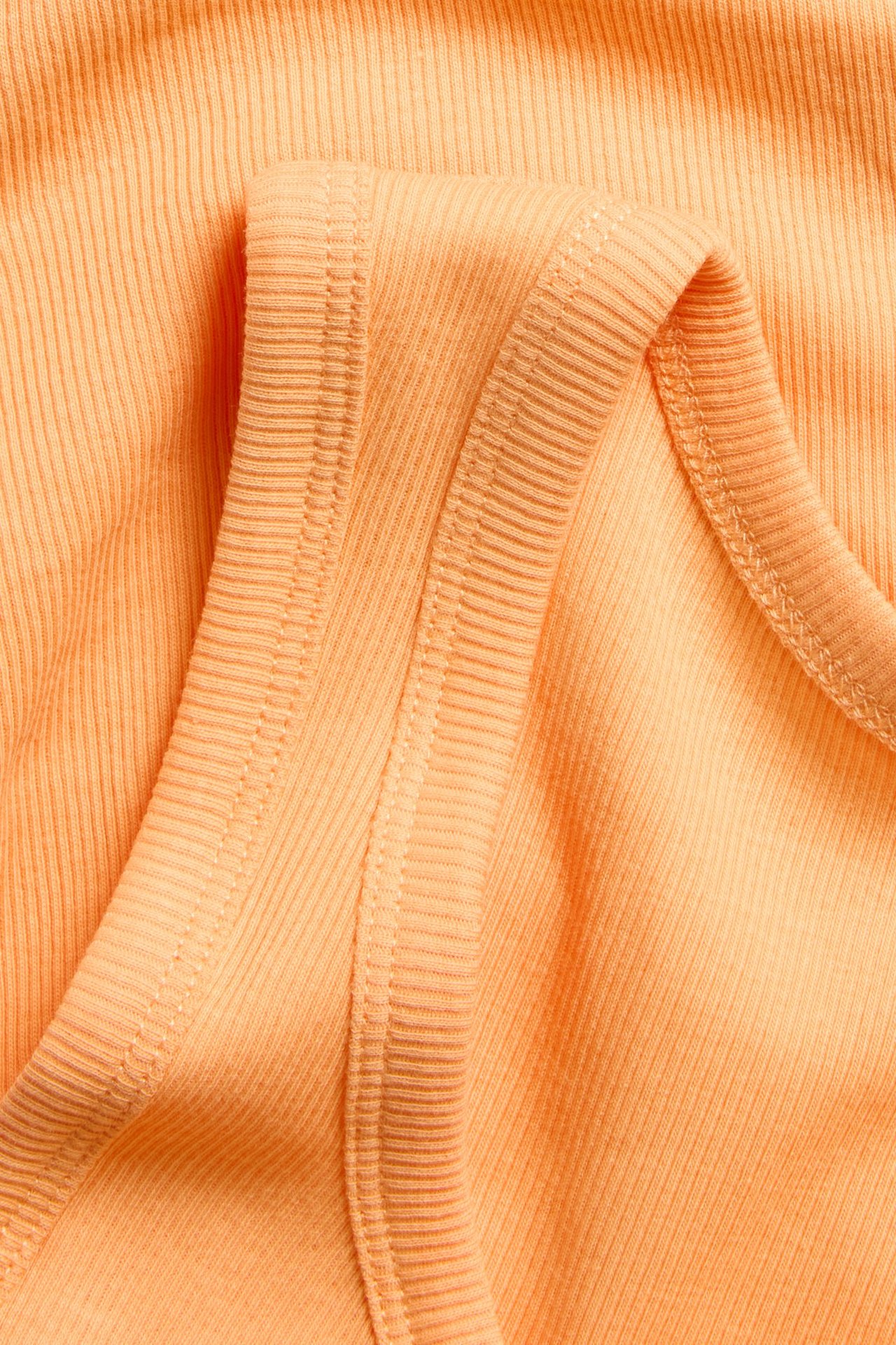 Nära bild av ett orange ribbat linne, som visar dess smala ribbstruktur och fina sömmar.