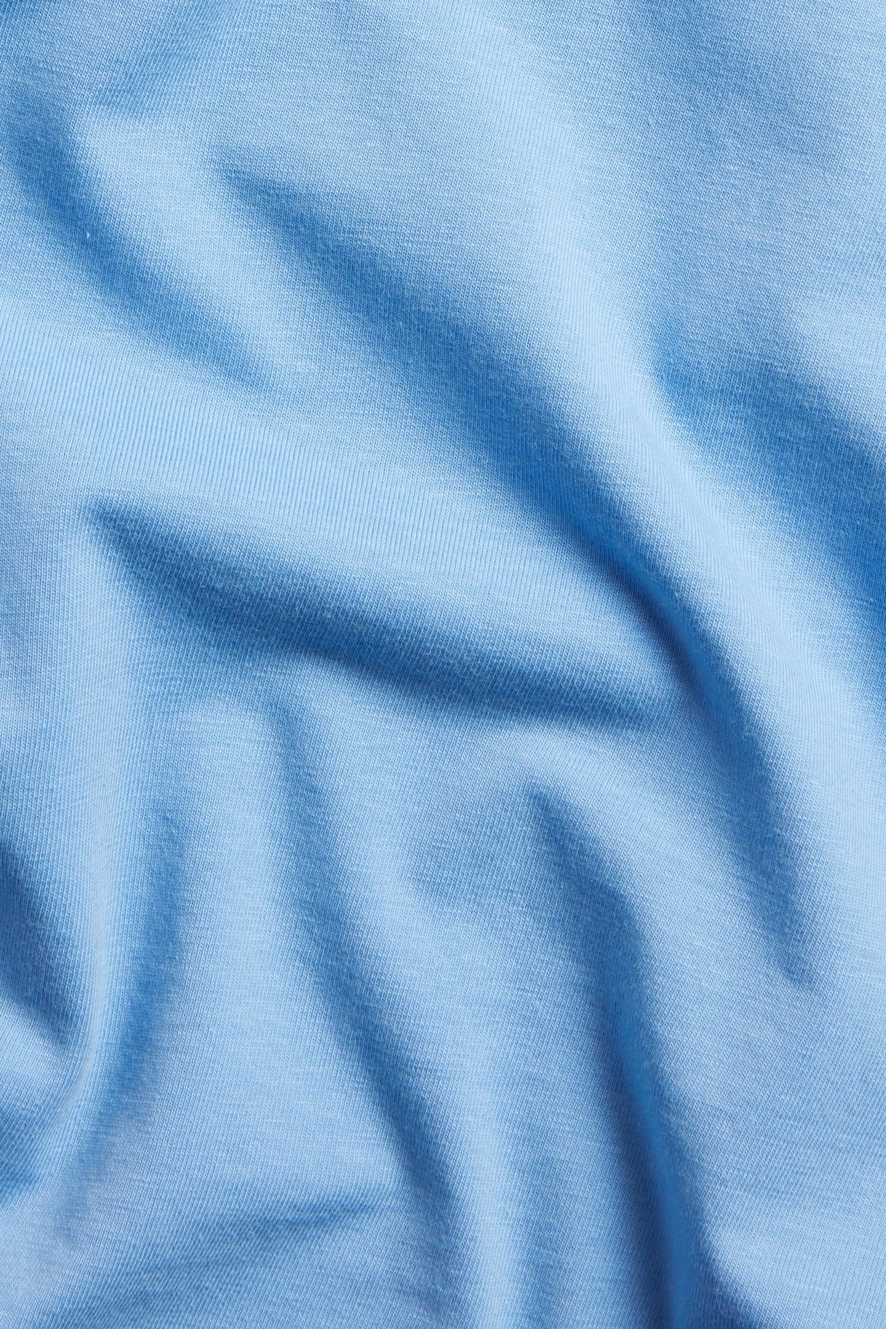 Zbliżenie na jasnoniebieski, długi rękaw, podstawowy top z dzianiny bawełnianej z widocznymi zagnieceniami.