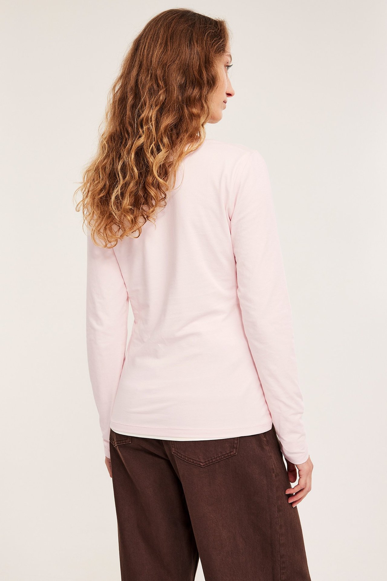 Ryggvisning av en kvinne i en lys rosa langermet basistopp og mørkebrune vide bukser.
