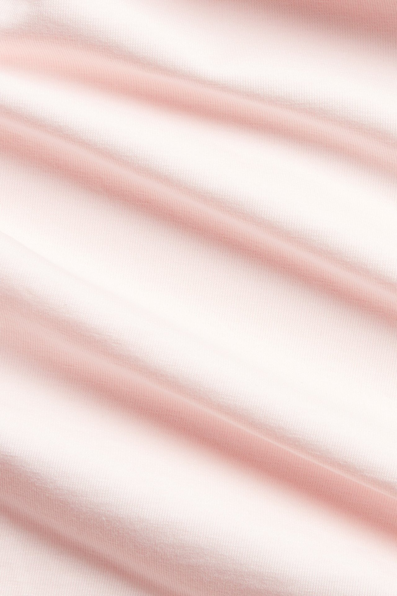 Zbliżenie na jasnoróżowy, jednolity materiał z mieszanki bawełny z delikatnymi fałdami, należący do bazowego topu.