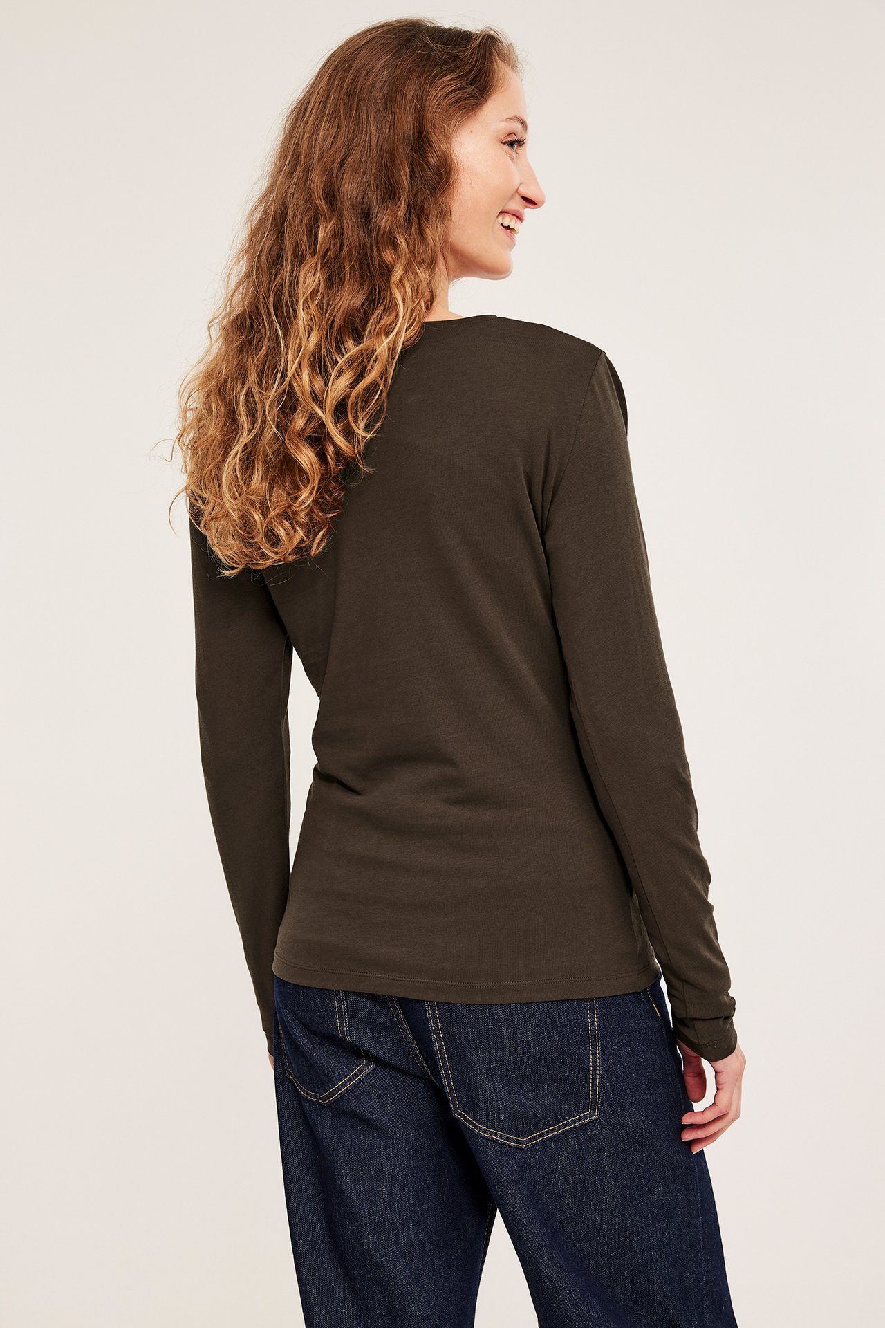 Kvinne sett bakfra i en mørkebrun langermet basistopp og mørkeblå jeans.