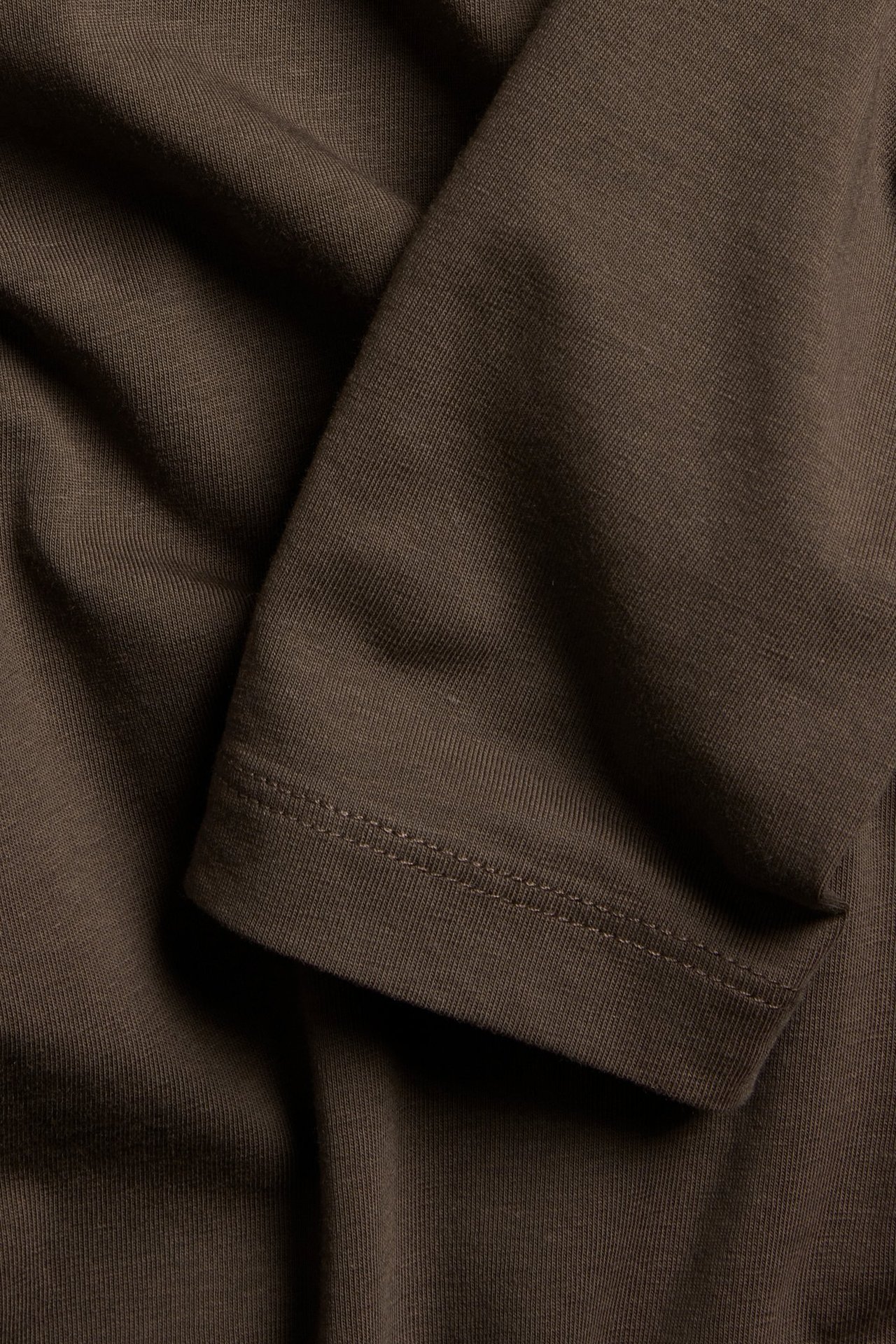 Zbliżenie ciemnobrązowego, długiego topu z widocznym prążkowanym mankietem.