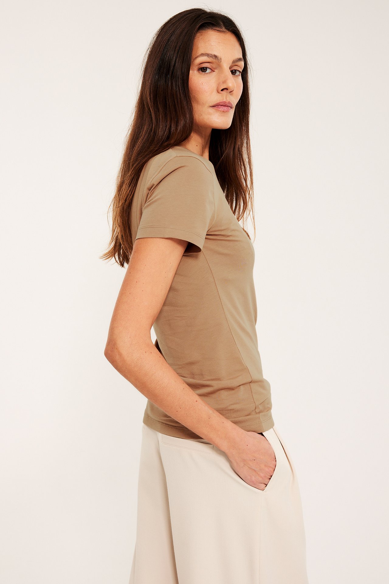 Sivukuva naisesta beigessä lyhythihaisessa pyöreäkauluksisessa perustopissa ja vaaleanbeigessä leveälahkeisissa housuissa.