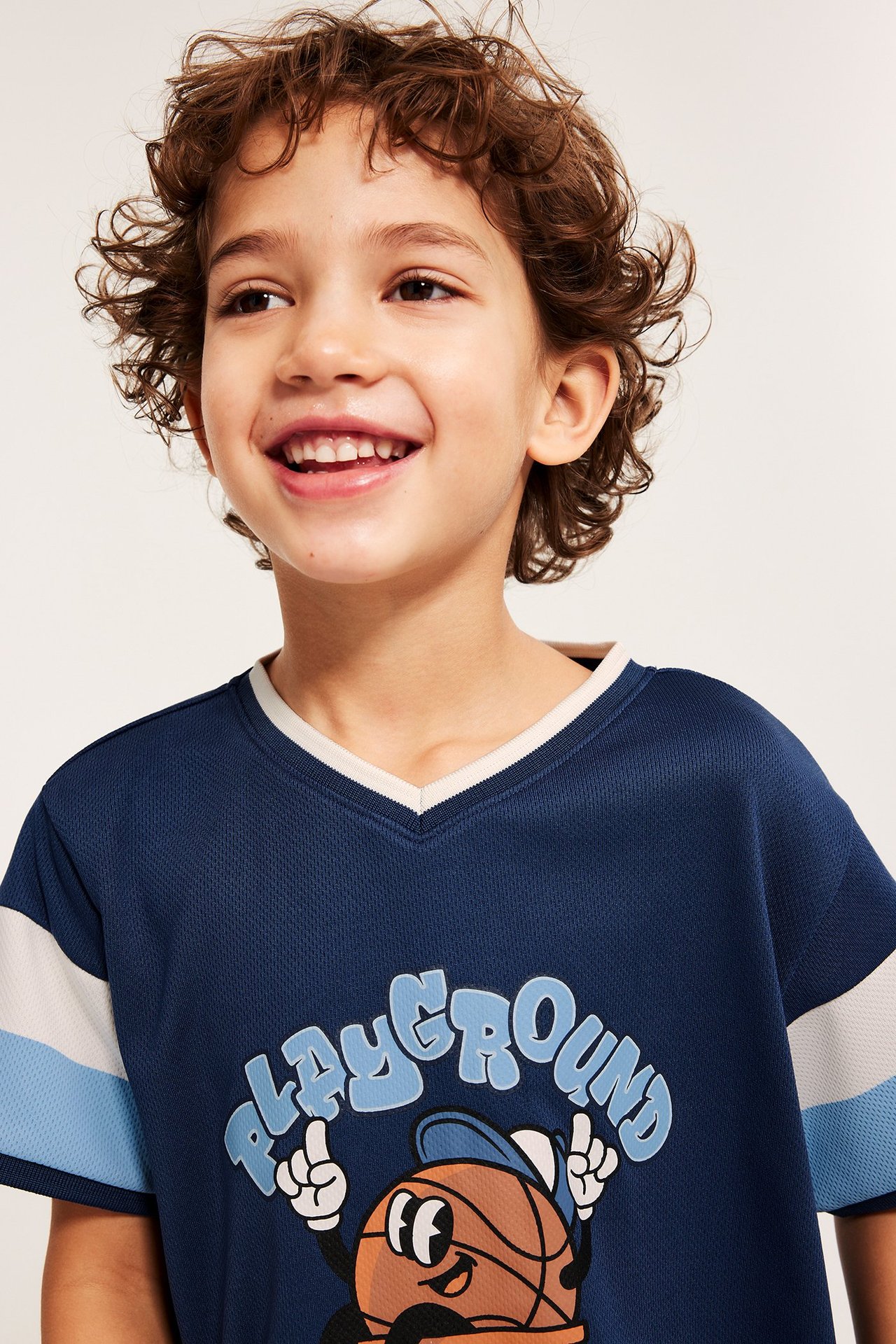 Nærbilde forfra, barn i mørkeblå mesh T-skjorte med 'PLAYGROUND'-trykk og stripete ermer.
