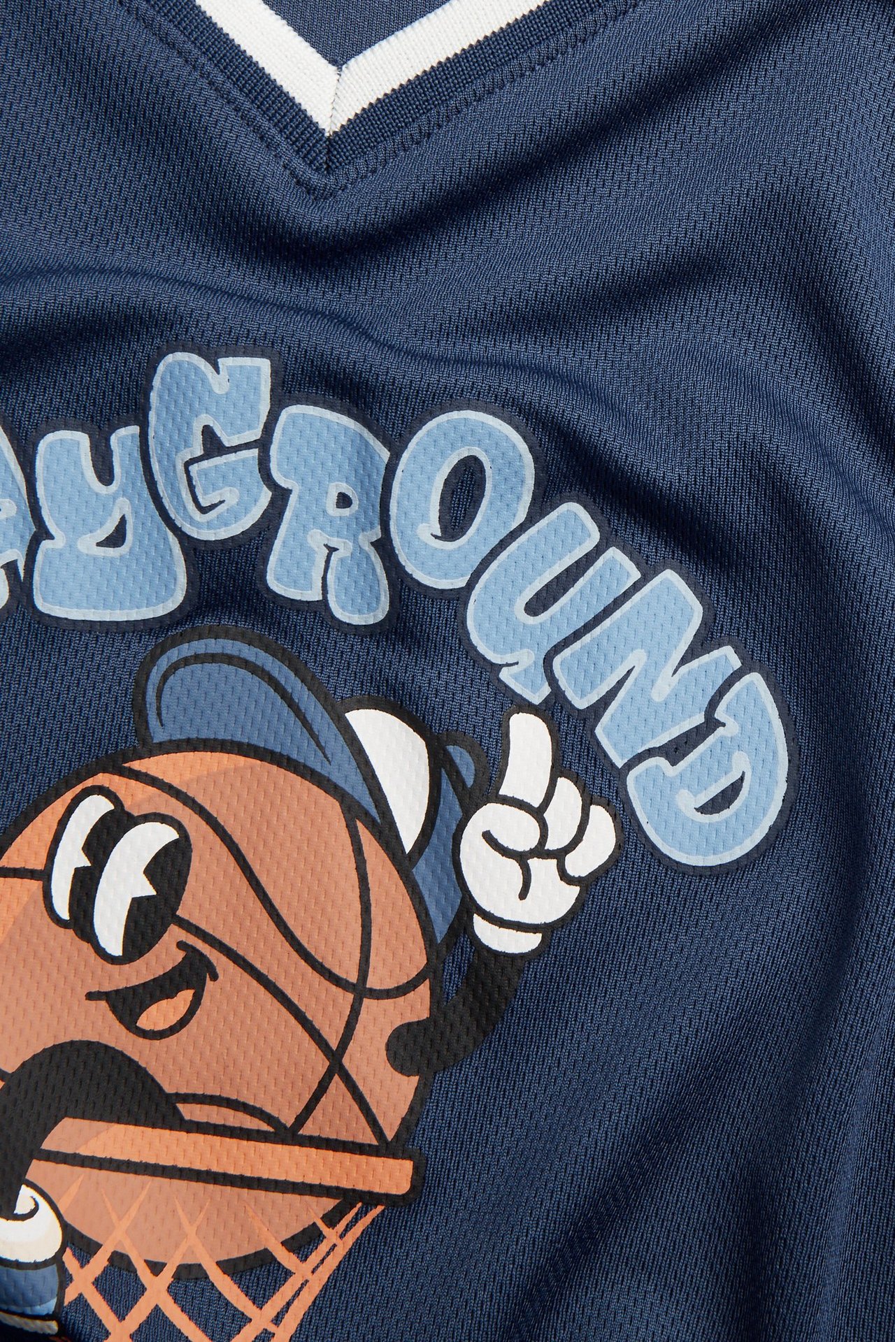 Zbliżenie niebieskiego T-shirtu z siateczki dla dzieci, prążkowany biały dekolt V, jasnoniebieski nadruk koszykówki.