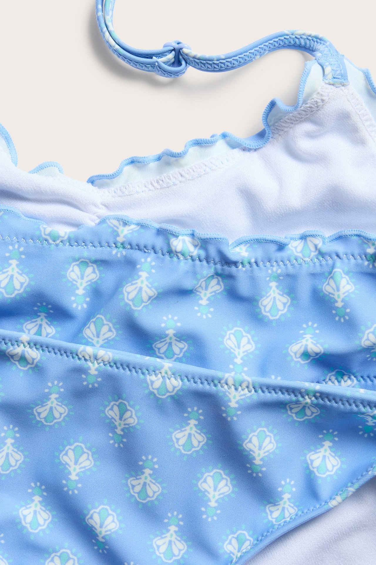 Zbliżenie niebieskiego, wzorzystego dziecięcego stanika bikini halterneck z białymi, jasnoniebieskimi wzorami muszli i falbankami.