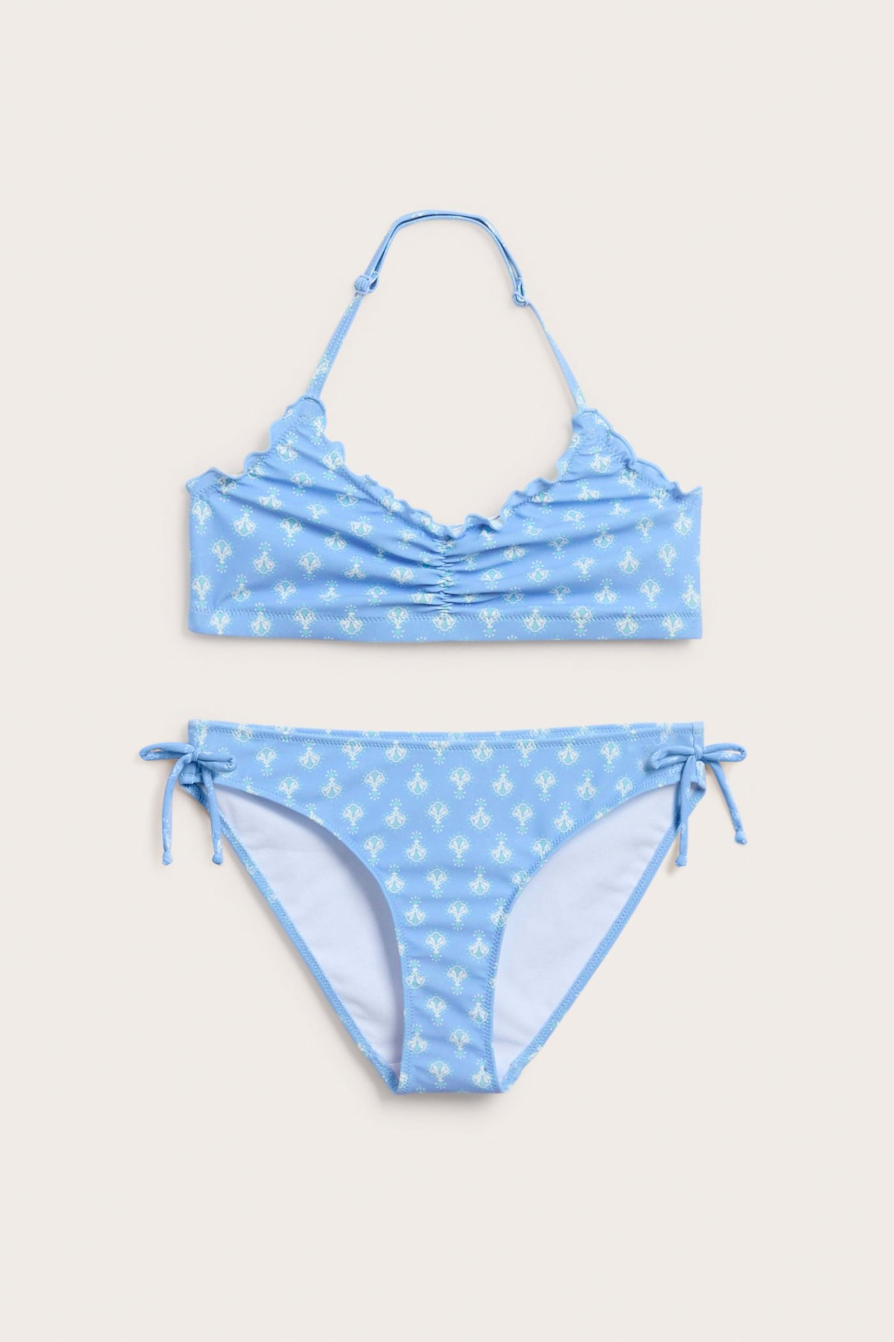 Frontvy av en blåmönstrad halterneck bikini för barn med rynkad topp och knytband i sidorna.