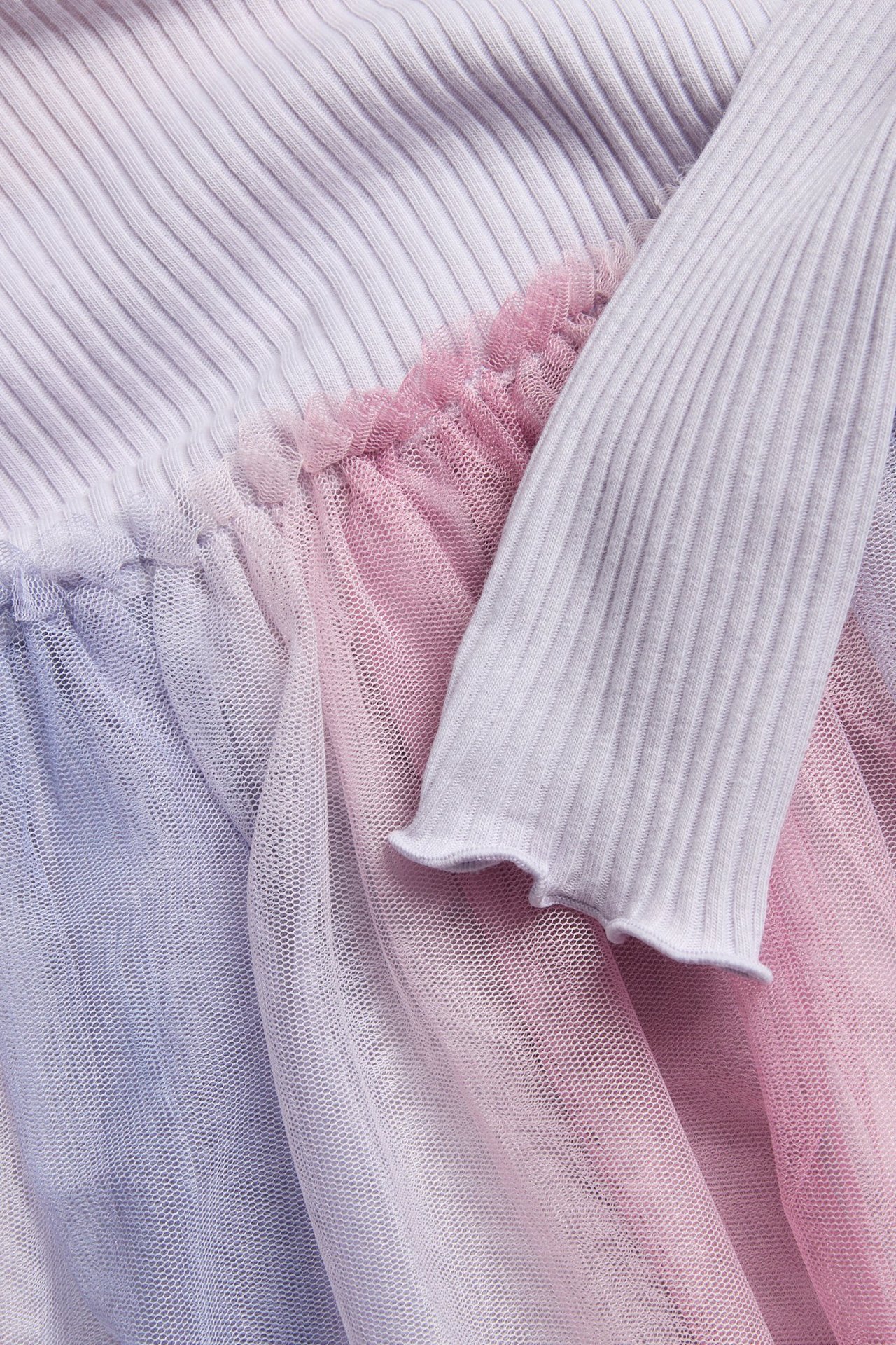 Zbliżenie sukienki dziecięcej w jasnofioletowy prążek z falbaniastym mankietem i marszczoną spódnicą z różowo-fioletowej siateczki.