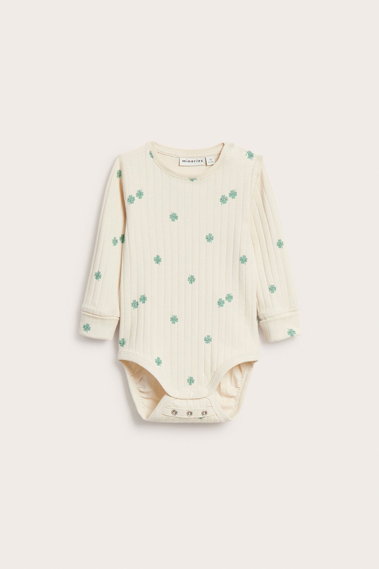 Frontvy av en beige ribbad långärmad babybody med grönt klövermönster och tryckknappar.
