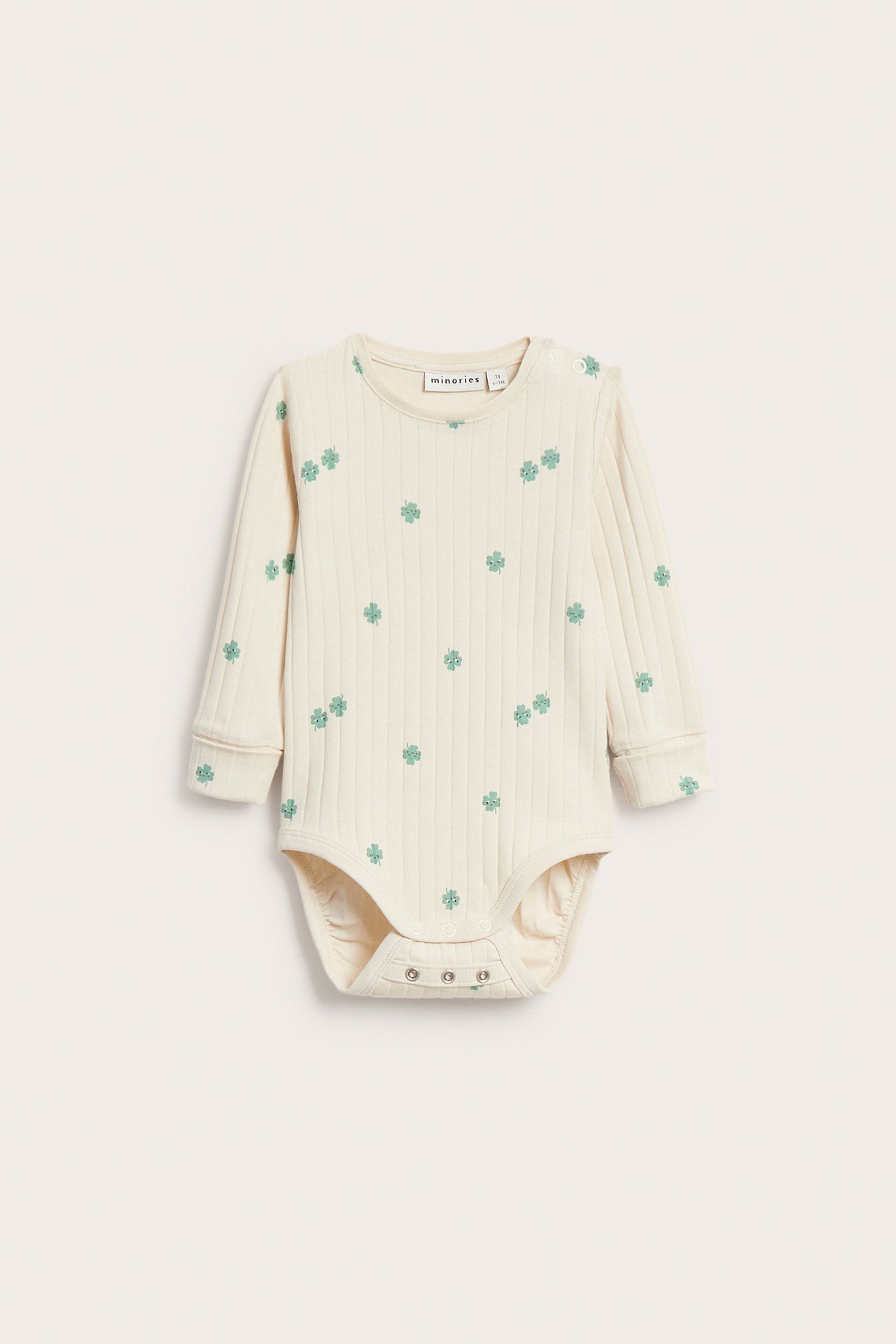 Frontvy av en beige ribbad långärmad babybody med grönt klövermönster och tryckknappar.