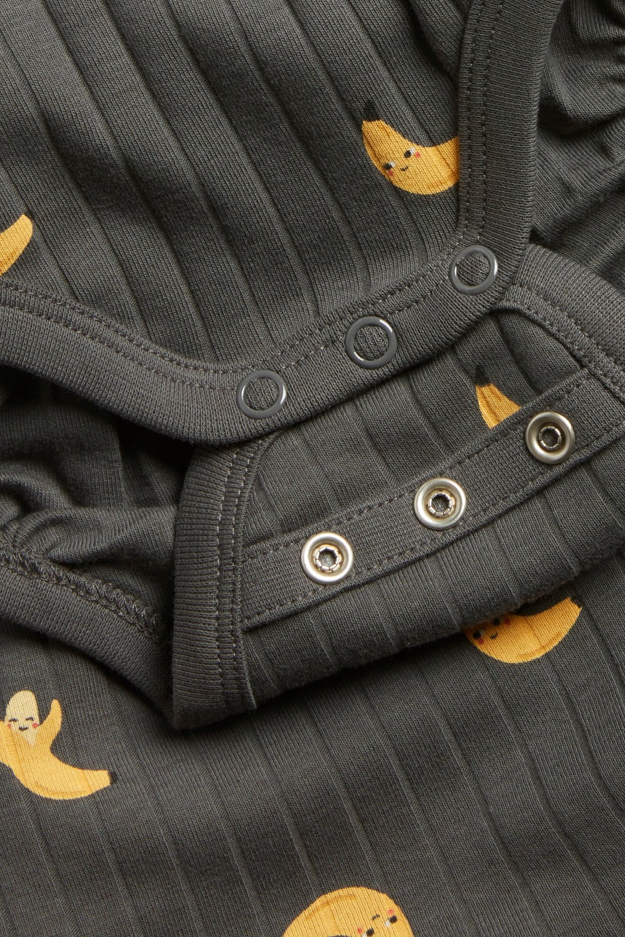 Lähikuva vauvan mustasta ribbibodysta, jossa on banaanikuvio ja nepparikiinnitys.