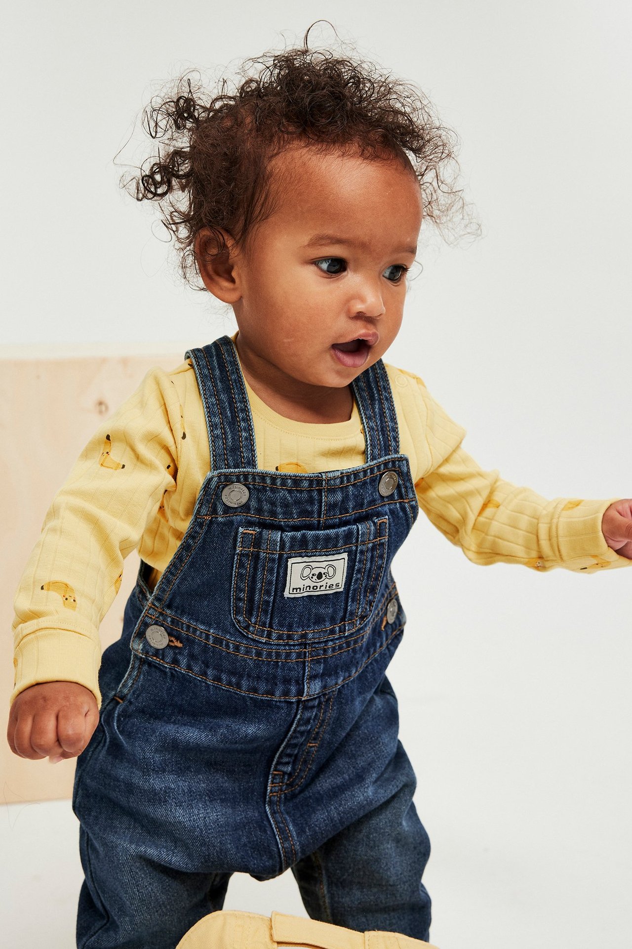Baby keltaisessa ribatussa pitkähihaisessa bodyassa hedelmäkuviolla tummien denimhaalareiden alla, edestä.