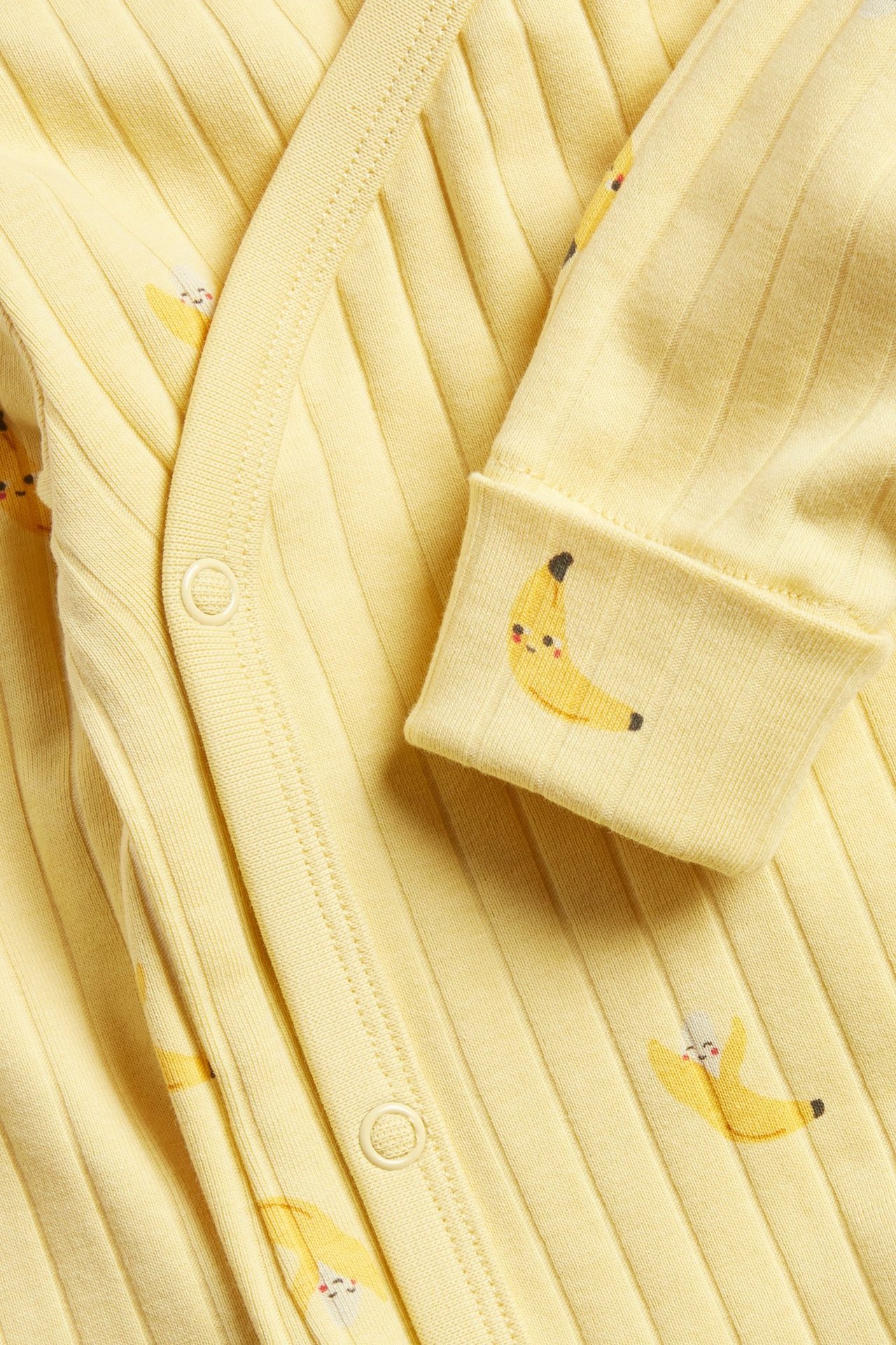 Zbliżenie żółtego prążkowanego body niemowlęcego z długim rękawem, nadrukiem bananów i zapięciem kopertowym.