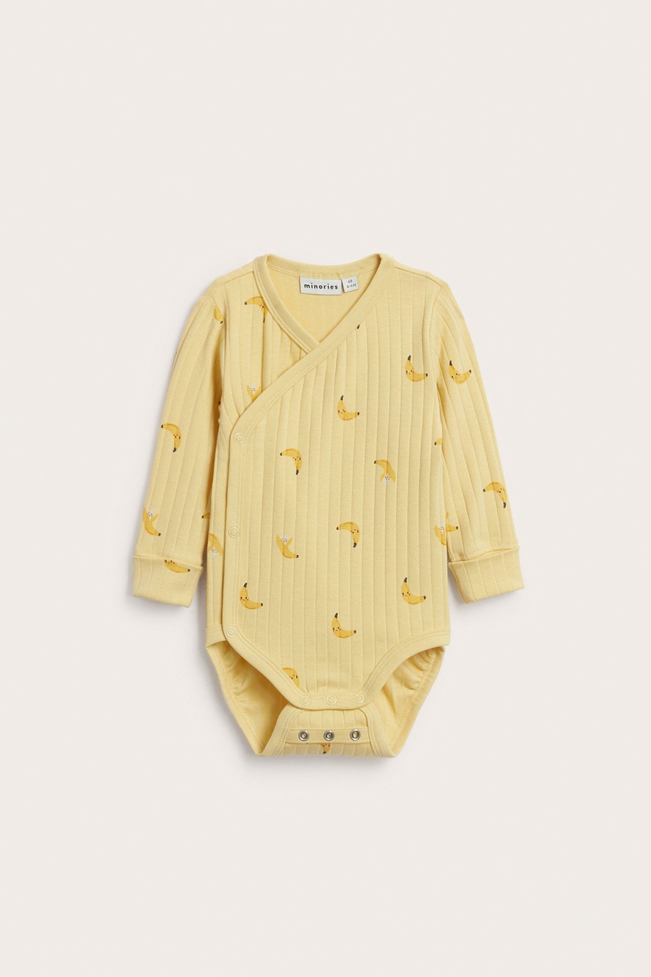 Edestä, keltainen, ribattu, pitkähihainen vauvan kietaisubody banaanikuviolla ja neppareilla.