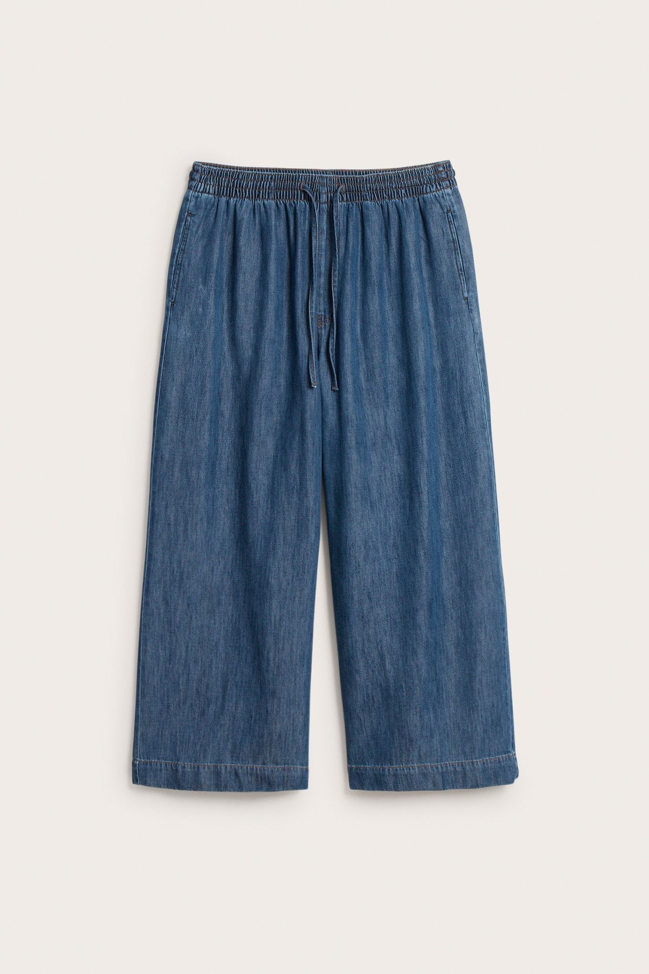 Etunäkymä tummansinisistä leveistä pull-on farkuista, joissa kiristysnyöri vyötäröllä ja sivutaskut.