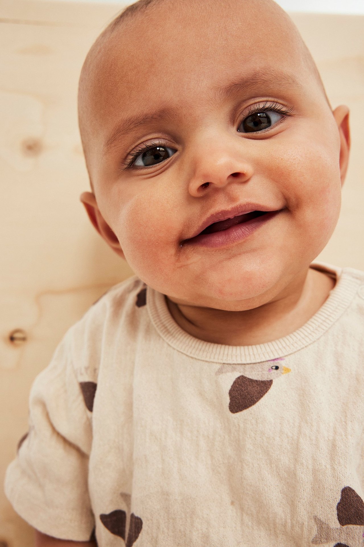 Närbild av en baby i en oversized beige bomullsbody med brunt fågelprint.
