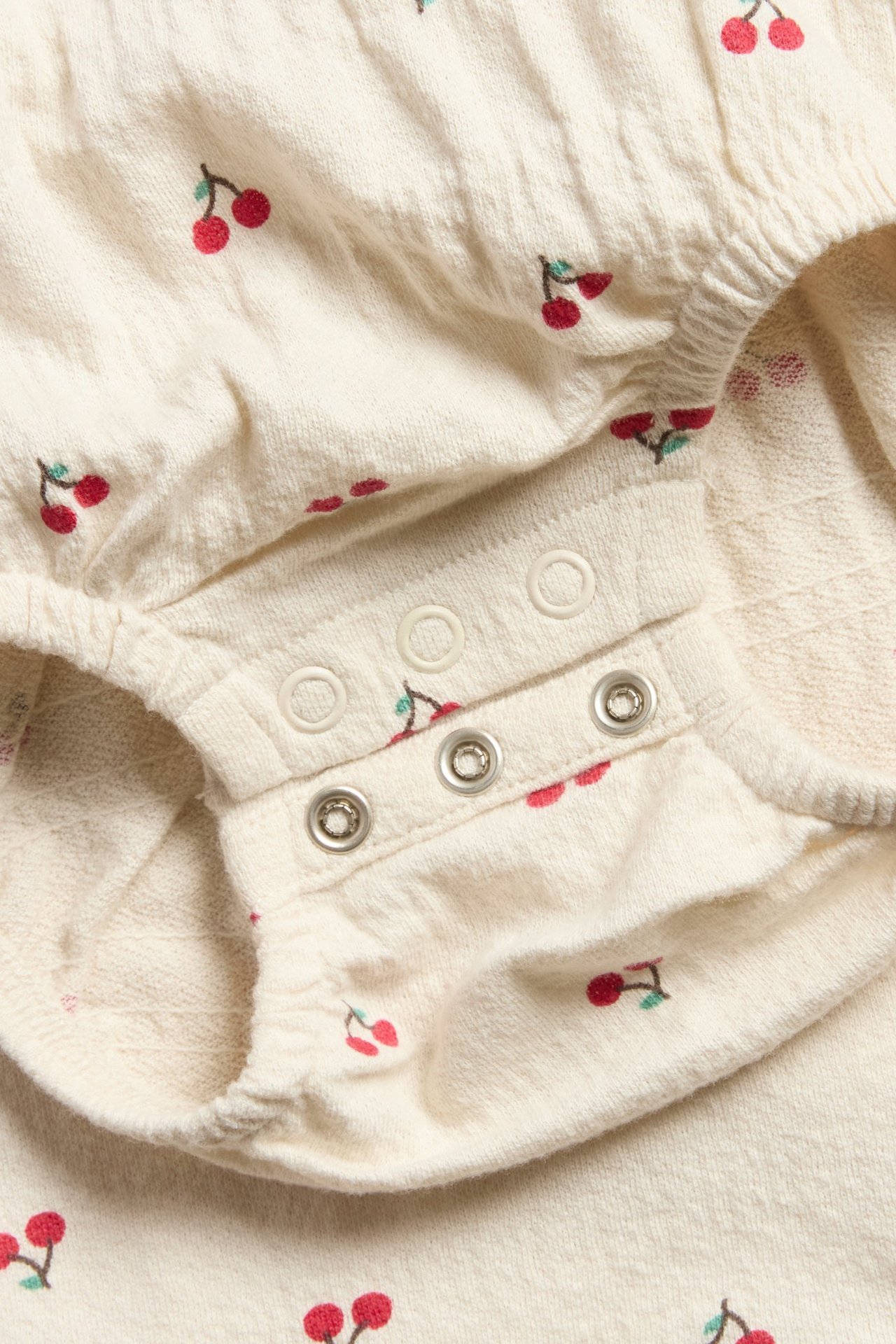 Lähikuva vauvan vaaleanbeigestä oversized bodysta, jossa on kirsikkaprintti ja painonapit.