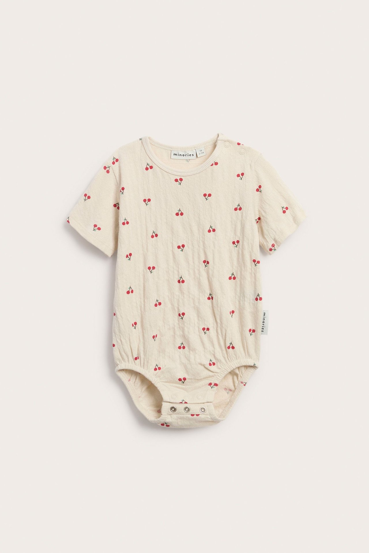 Widok z przodu na beżowe body niemowlęce oversize z wiśniowym wzorem, zatrzaski na ramieniu i w kroku.