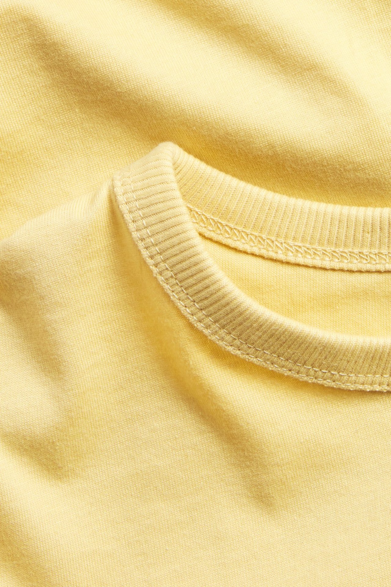 Zbliżenie na żółtą bawełnianą koszulkę z krótkim rękawem i prążkowanym okrągłym dekoltem.