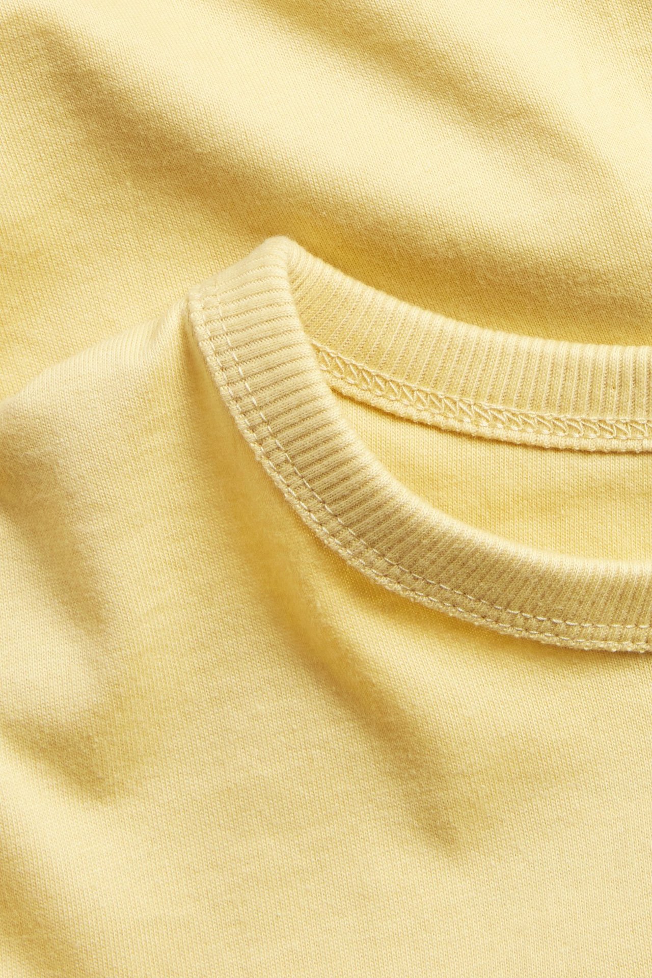 Zbliżenie jednolitego żółtego bawełnianego t-shirtu z krótkim rękawem i prążkowanym okrągłym dekoltem.